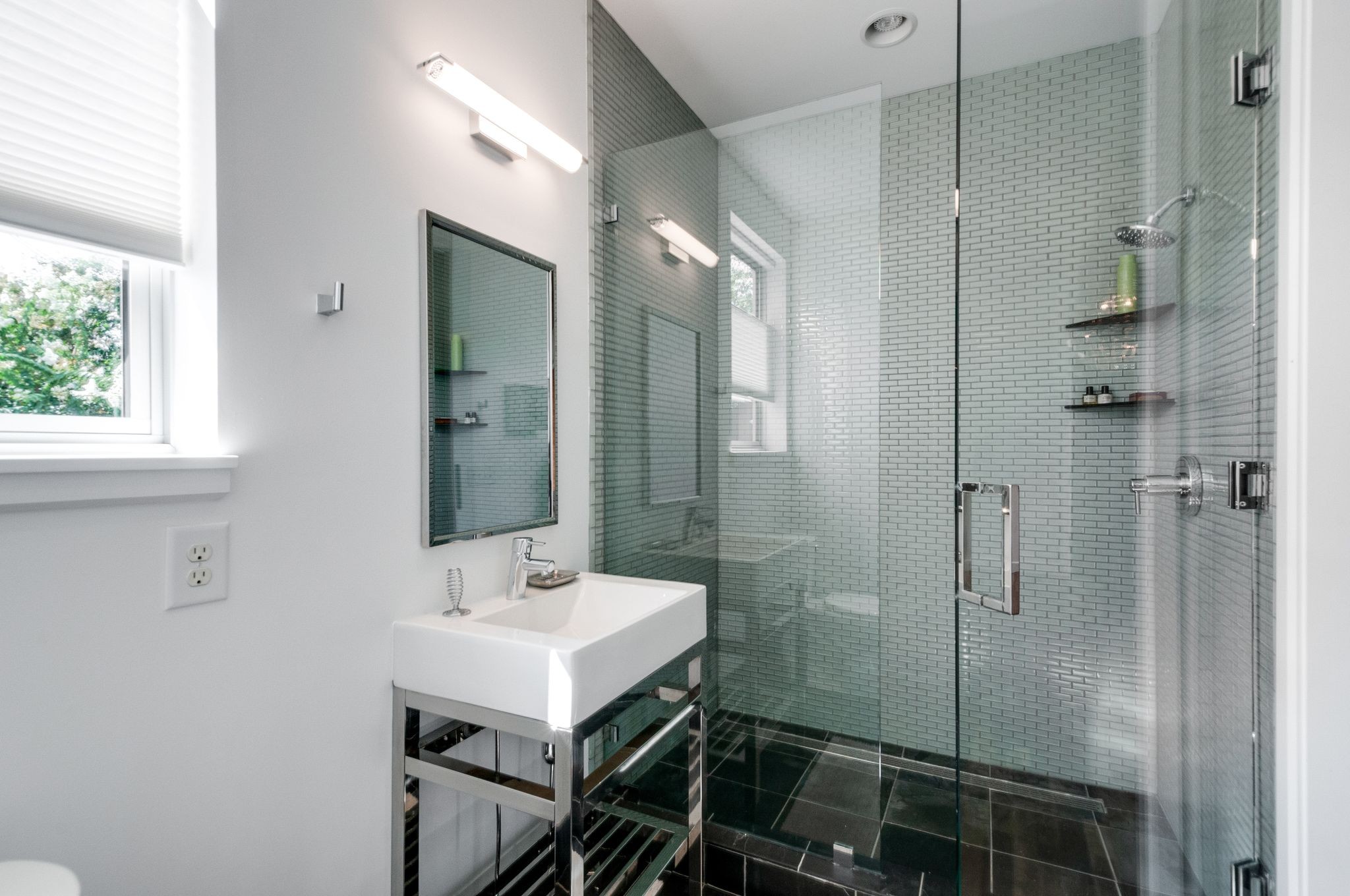 Modern bathroom with a glass shower, pale tile, and a white sink on a chrome vanity.