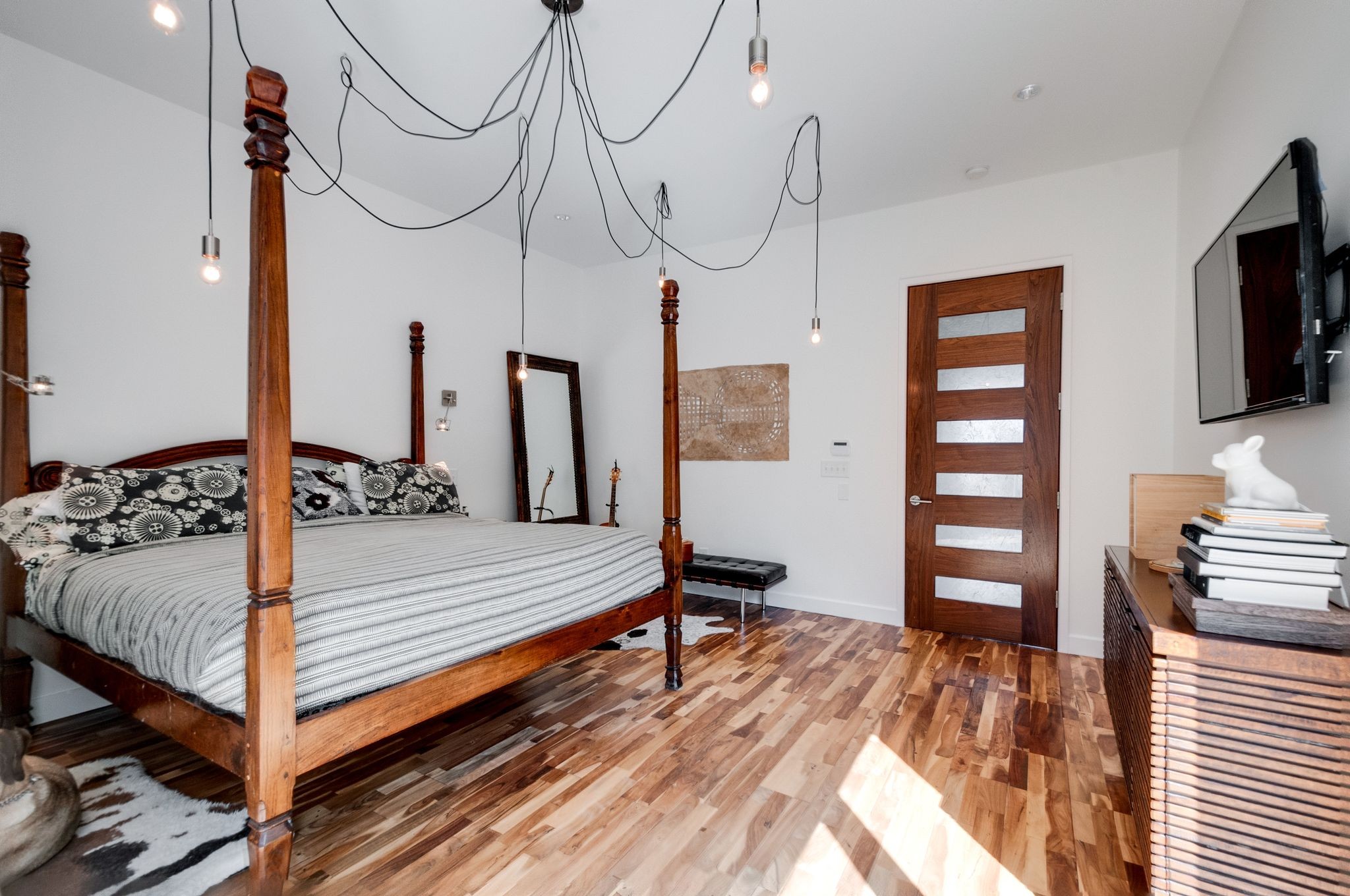 Bedroom with a wooden four-poster bed, exposed pendant bulbs, and mixed-tone wood flooring.
