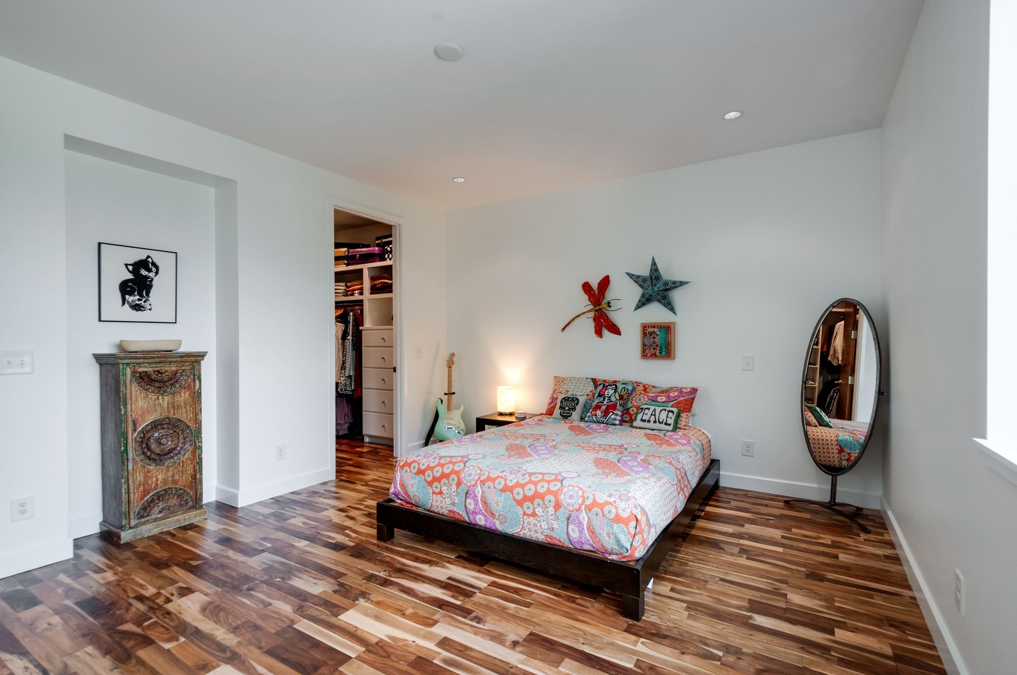 Bedroom with a colorful patterned quilt, dark wood floors, open closet, and guitar.