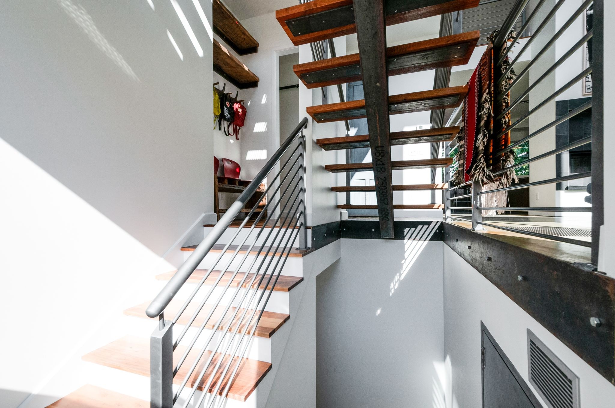 Modern stairwell with open wood stairs, dark metal railings, and scarves hanging above.