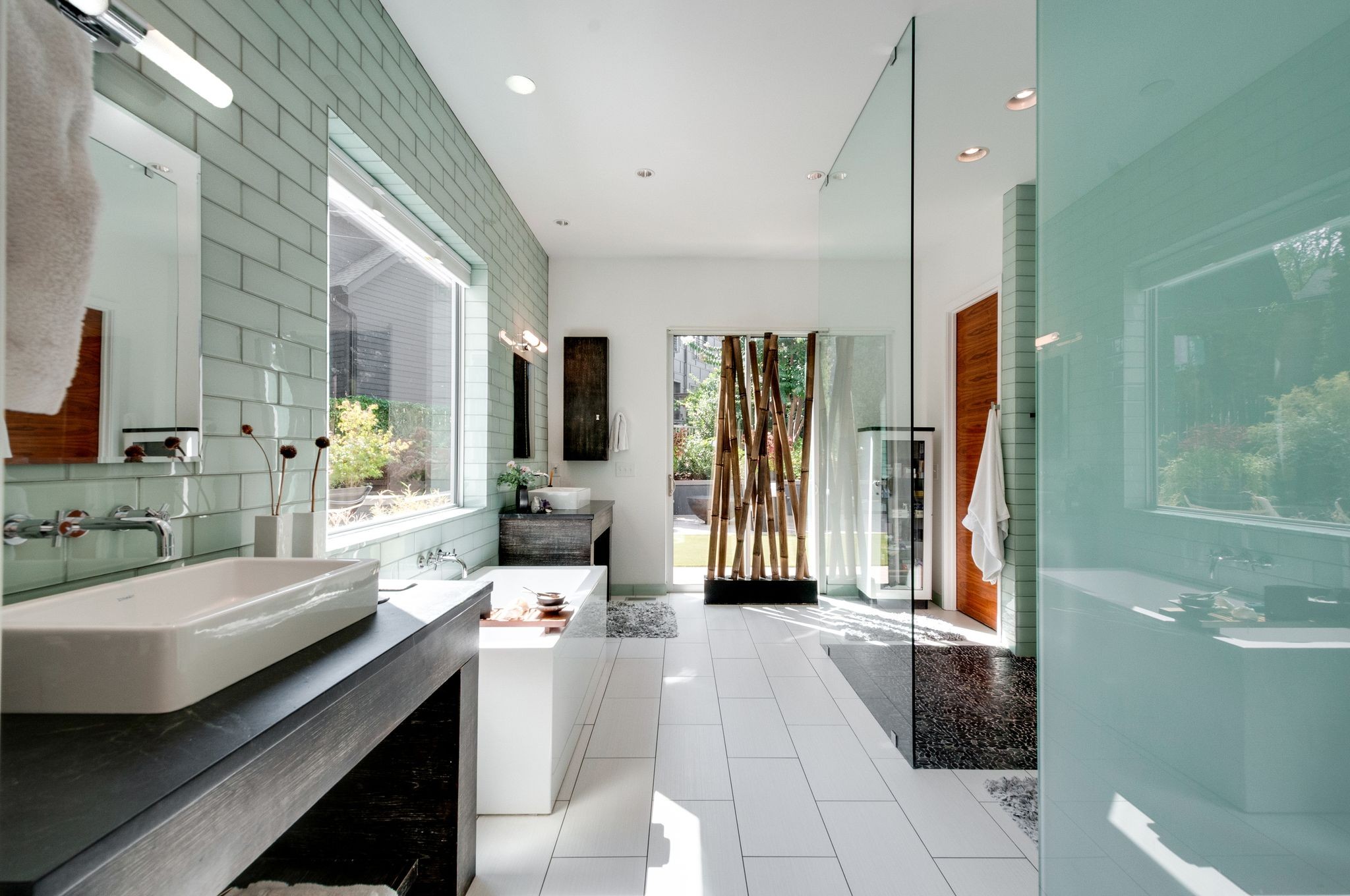 Modern bathroom with a freestanding tub, green tile, glass shower, and wooden screen by the garden doorway.