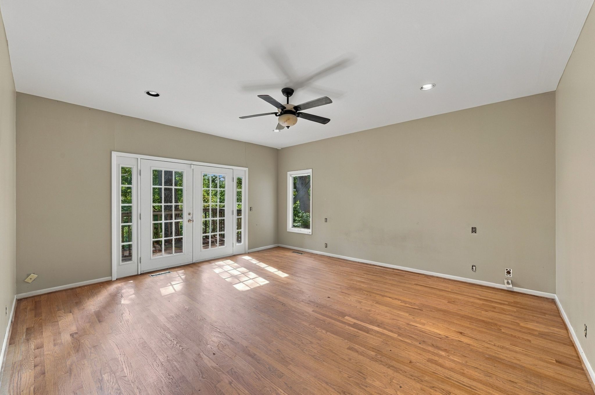 Empty room with hardwood floors, a ceiling fan, and French doors opening onto a deck.