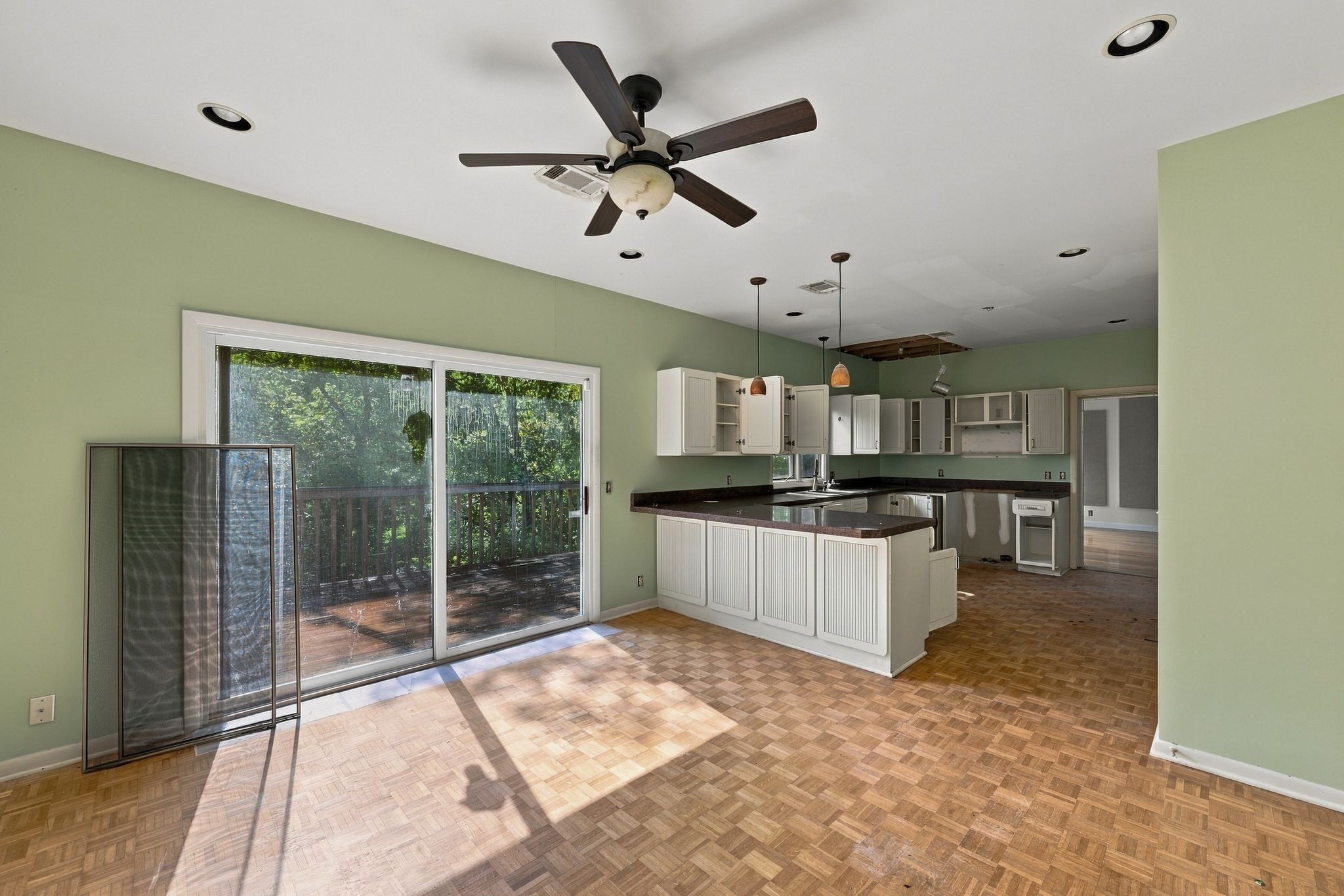 Vacant kitchen with open cabinets, parquet flooring, and sliding doors to a tree-lined deck.