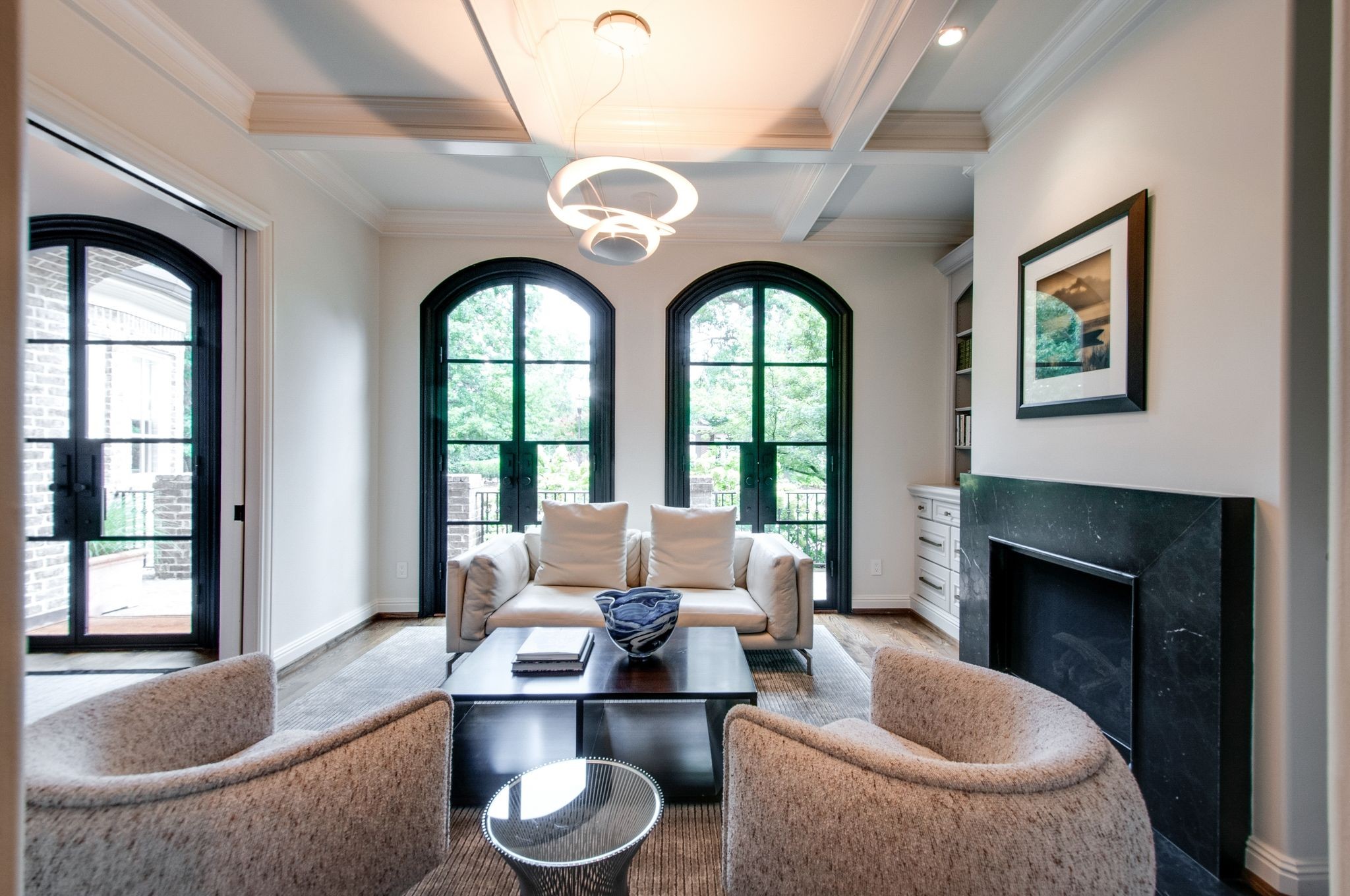 Living room with a dark stone fireplace, arched black-framed windows, and a cream sofa between two armchairs.