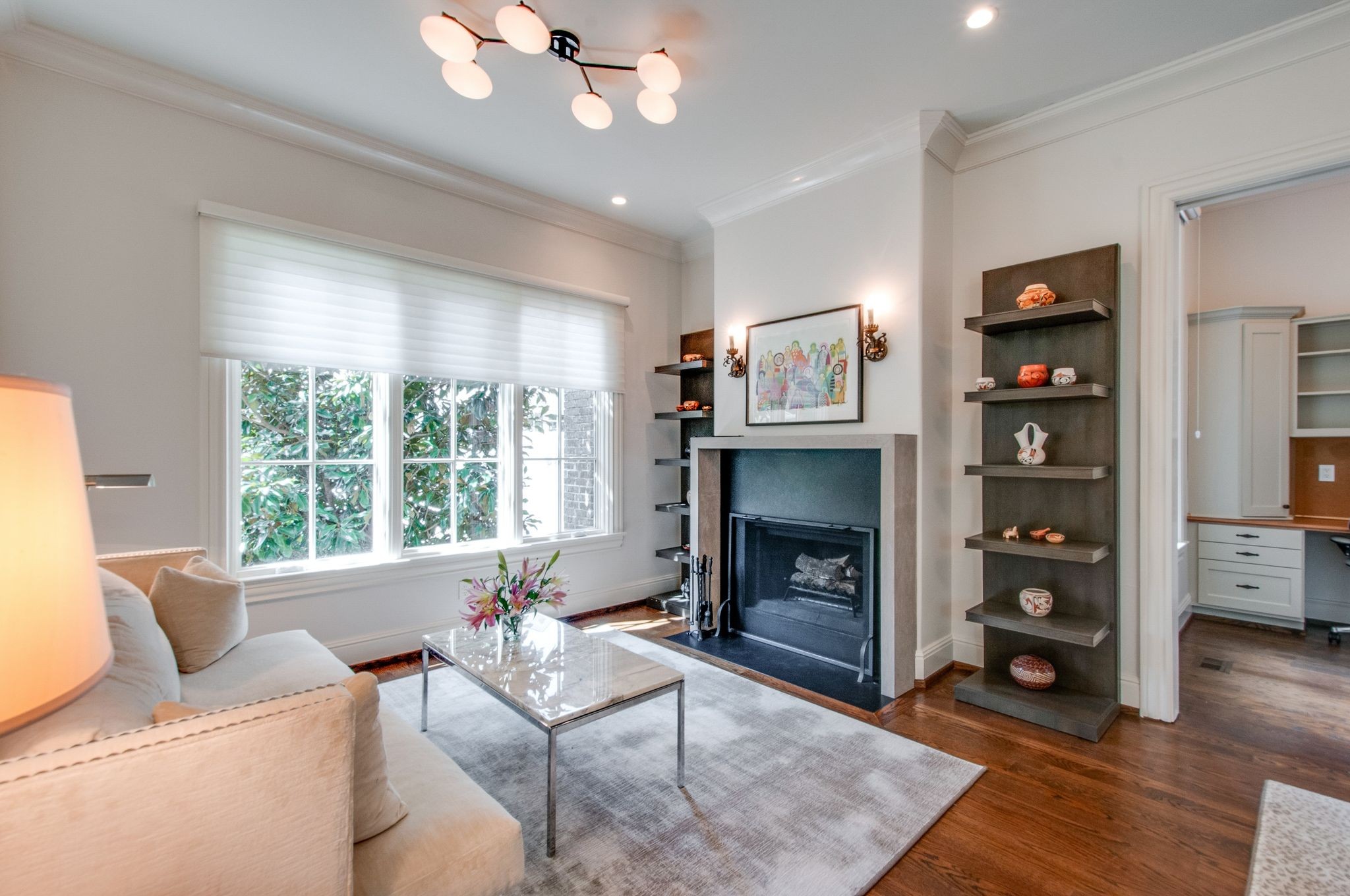 Living room with a fireplace, built-in shelves, and a large window beside a cream sofa.