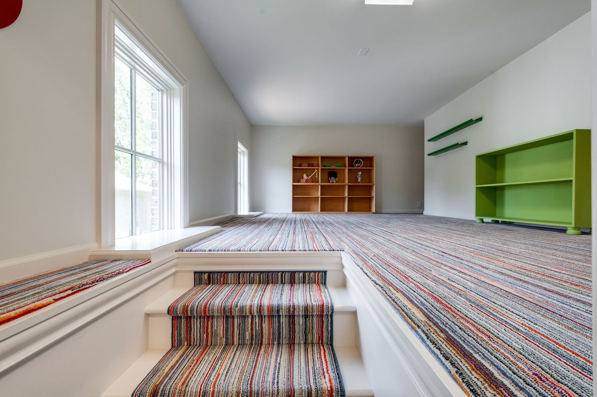 Playroom with striped carpeted steps leading to a raised area with a green cabinet and cubby shelves.