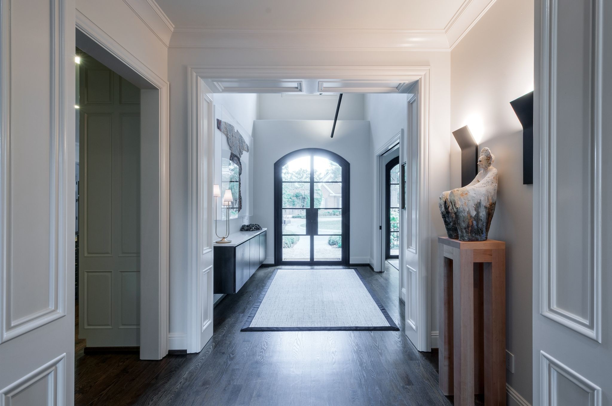 Entry hall with dark hardwood floors, a pale runner, and arched black-framed glass doors.