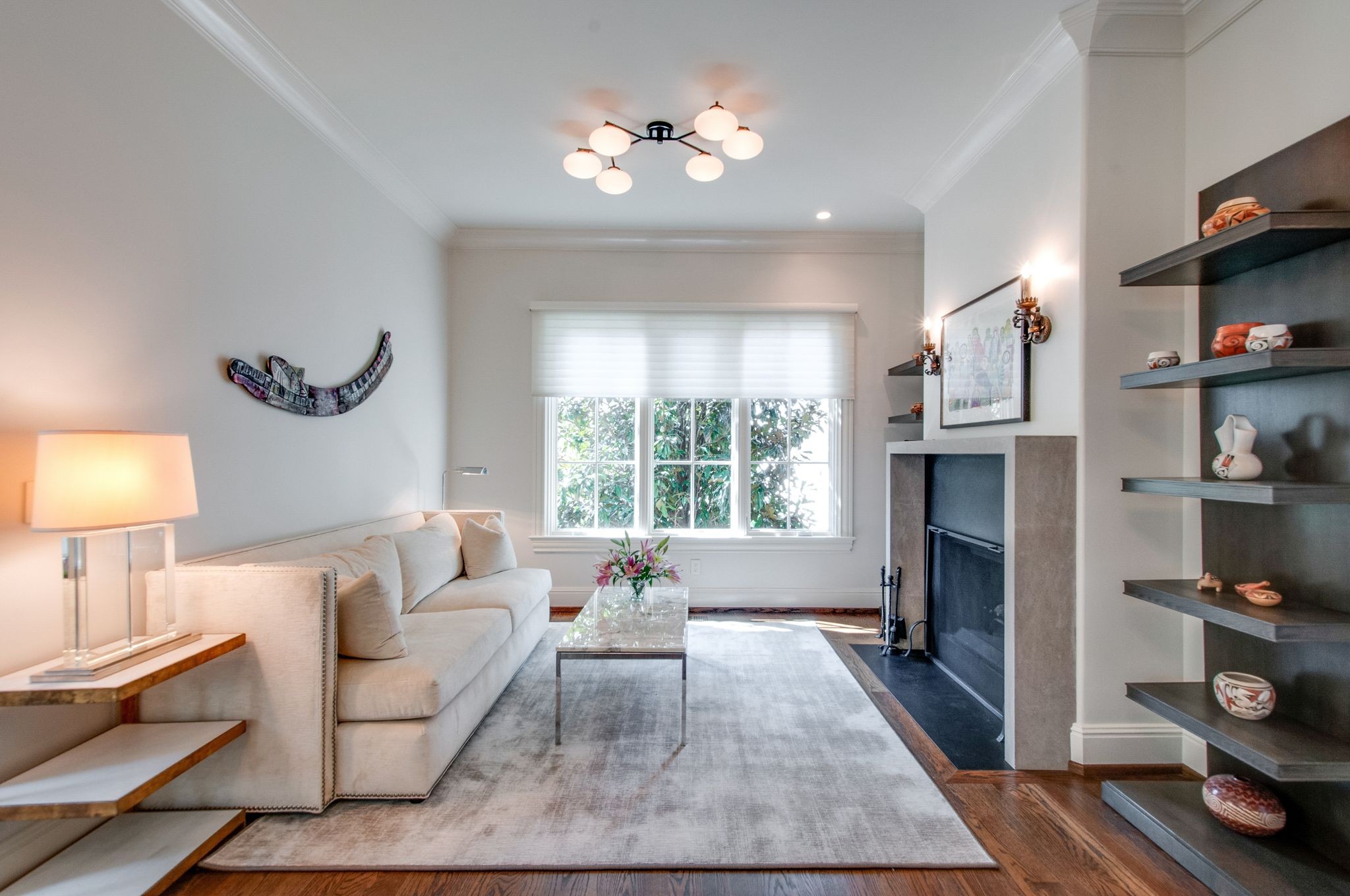 Living room with a cream sofa, fireplace, and built-in display shelves beside a large window.