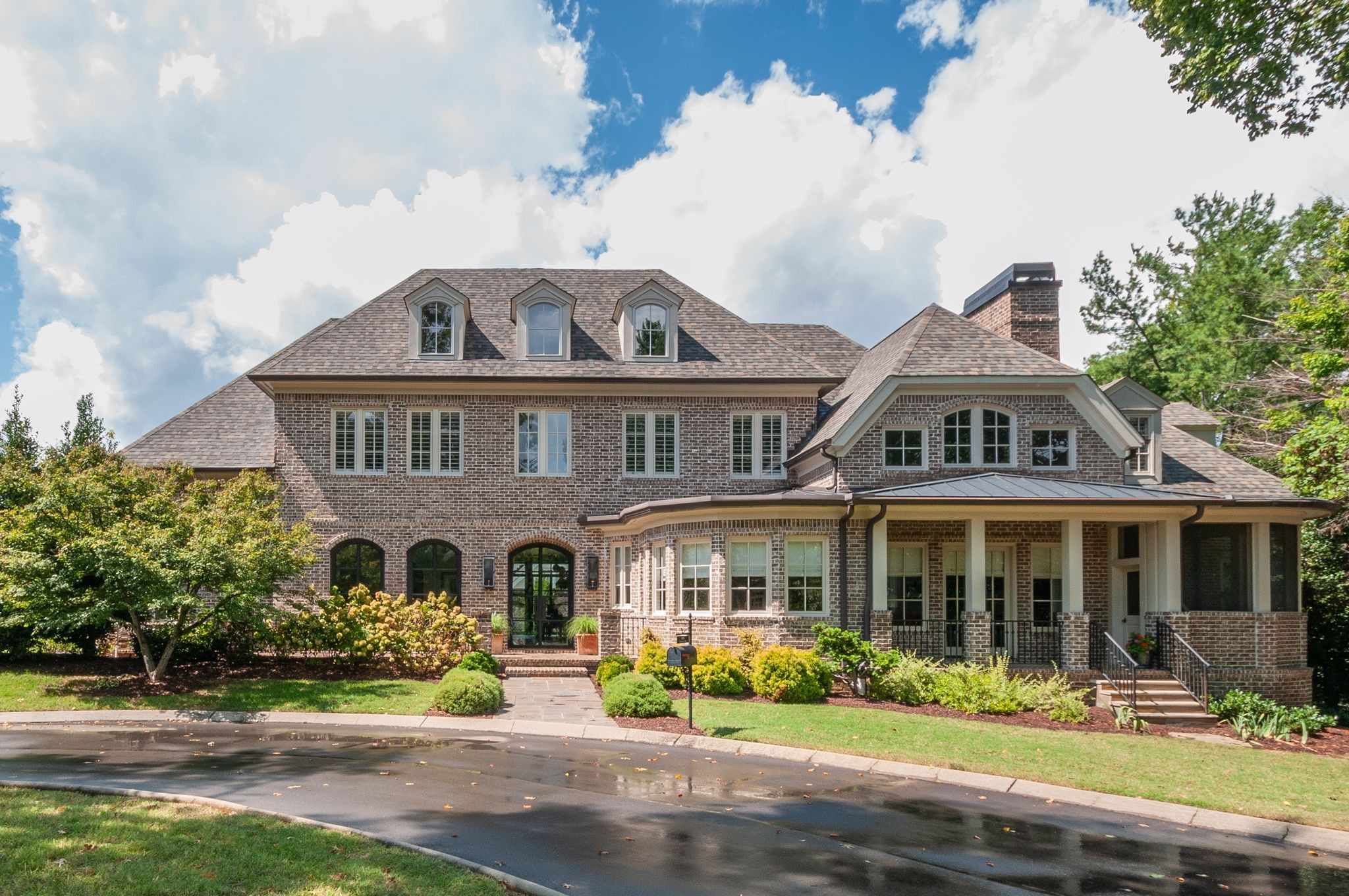 Two-story brick house with roof dormers, a covered porch, and landscaped front yard.