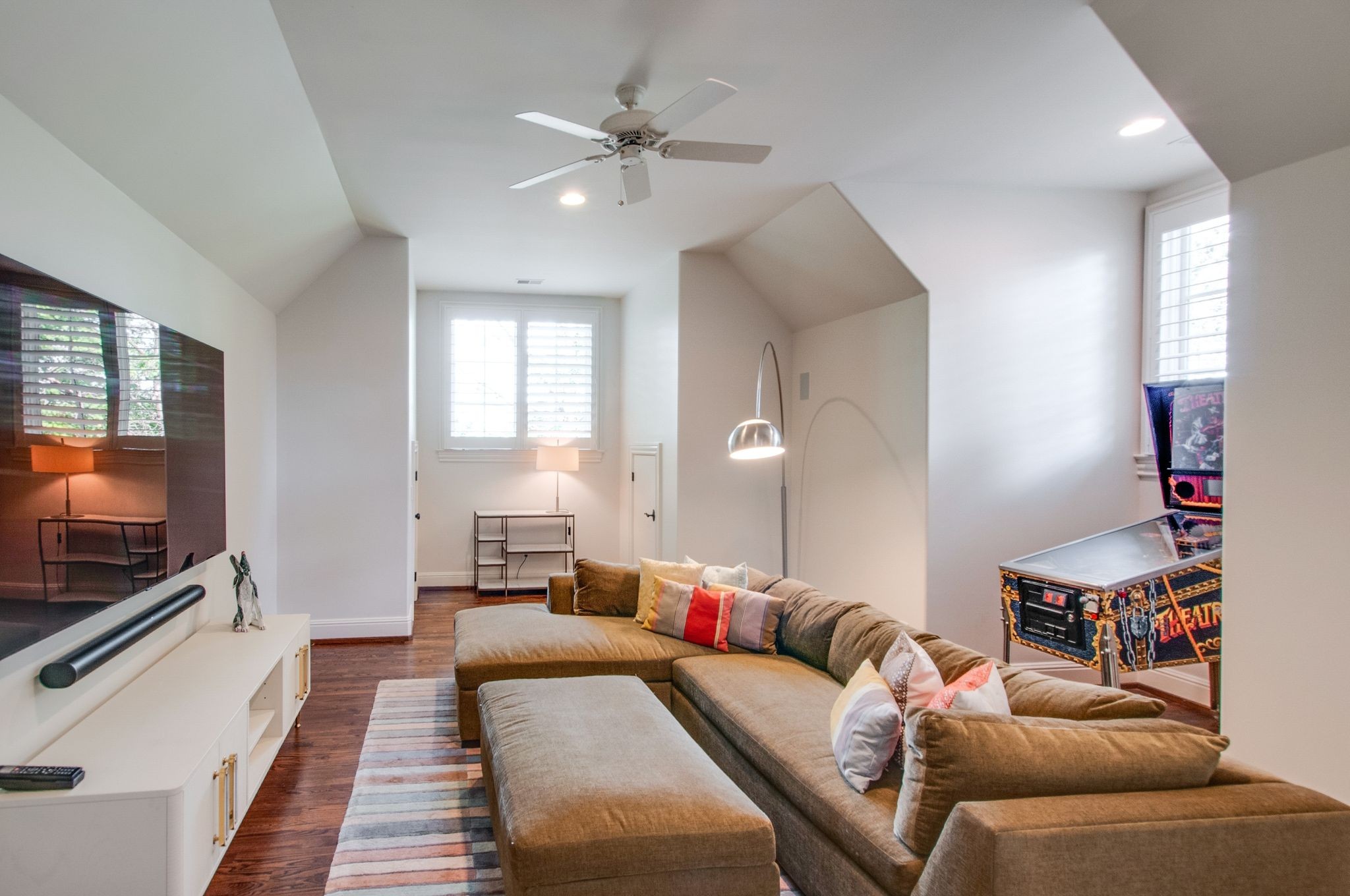 Media room with a large sectional sofa, wall-mounted television, and pinball machine.