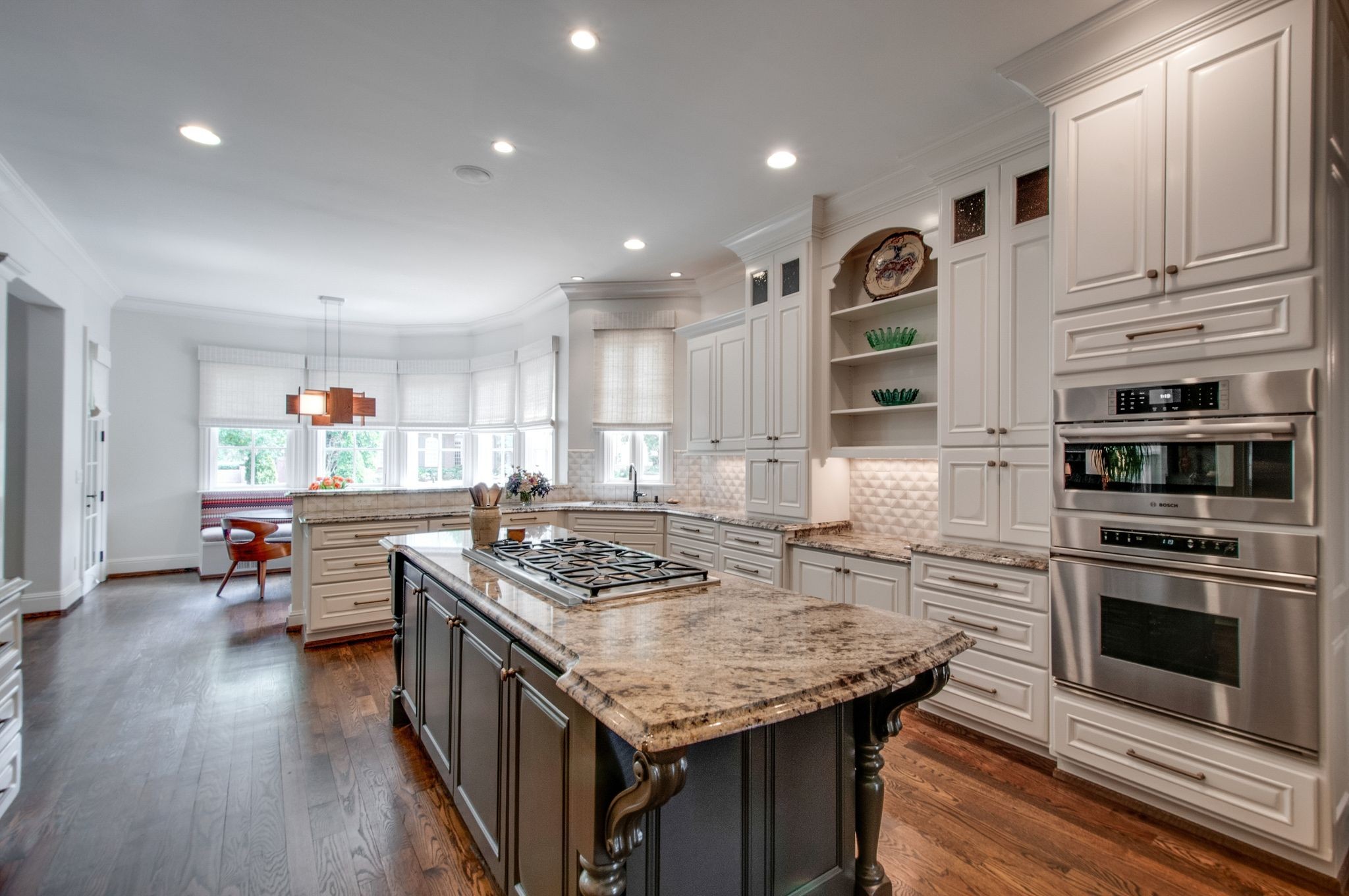 Bright kitchen with a large granite island, gas cooktop, white cabinetry, and stainless steel double ovens.