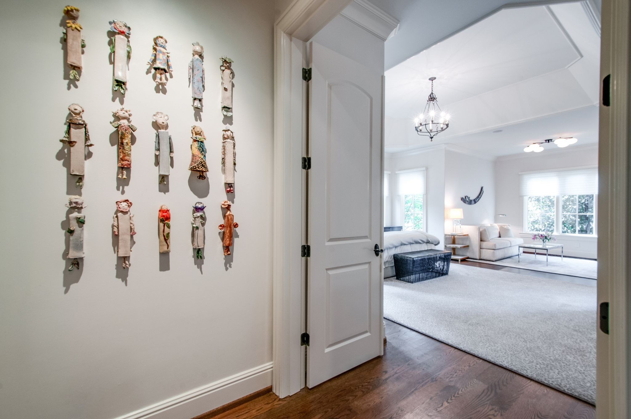 Furnished bedroom and sitting area seen through a doorway, with handmade wall figures and a chandelier.