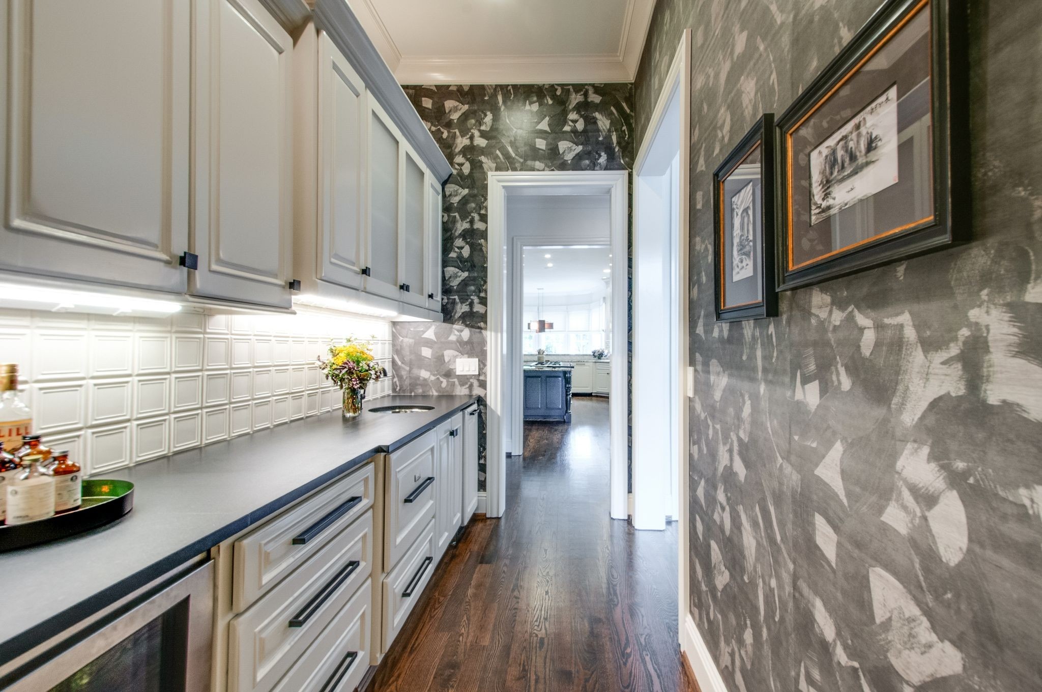 Butler’s pantry with white cabinetry, gray countertop, patterned wallpaper, and a view into the kitchen.