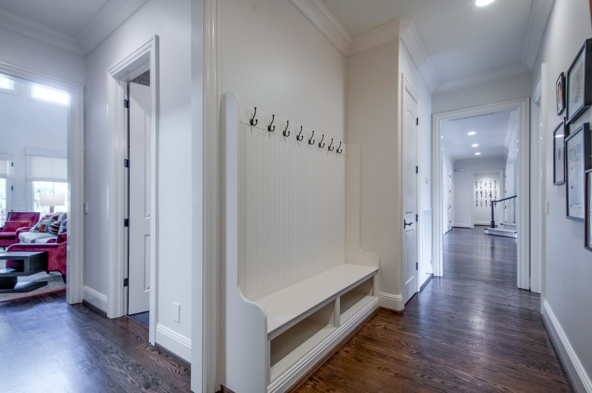 Entry hall with a built-in white bench and coat hooks beside a dark hardwood hallway.