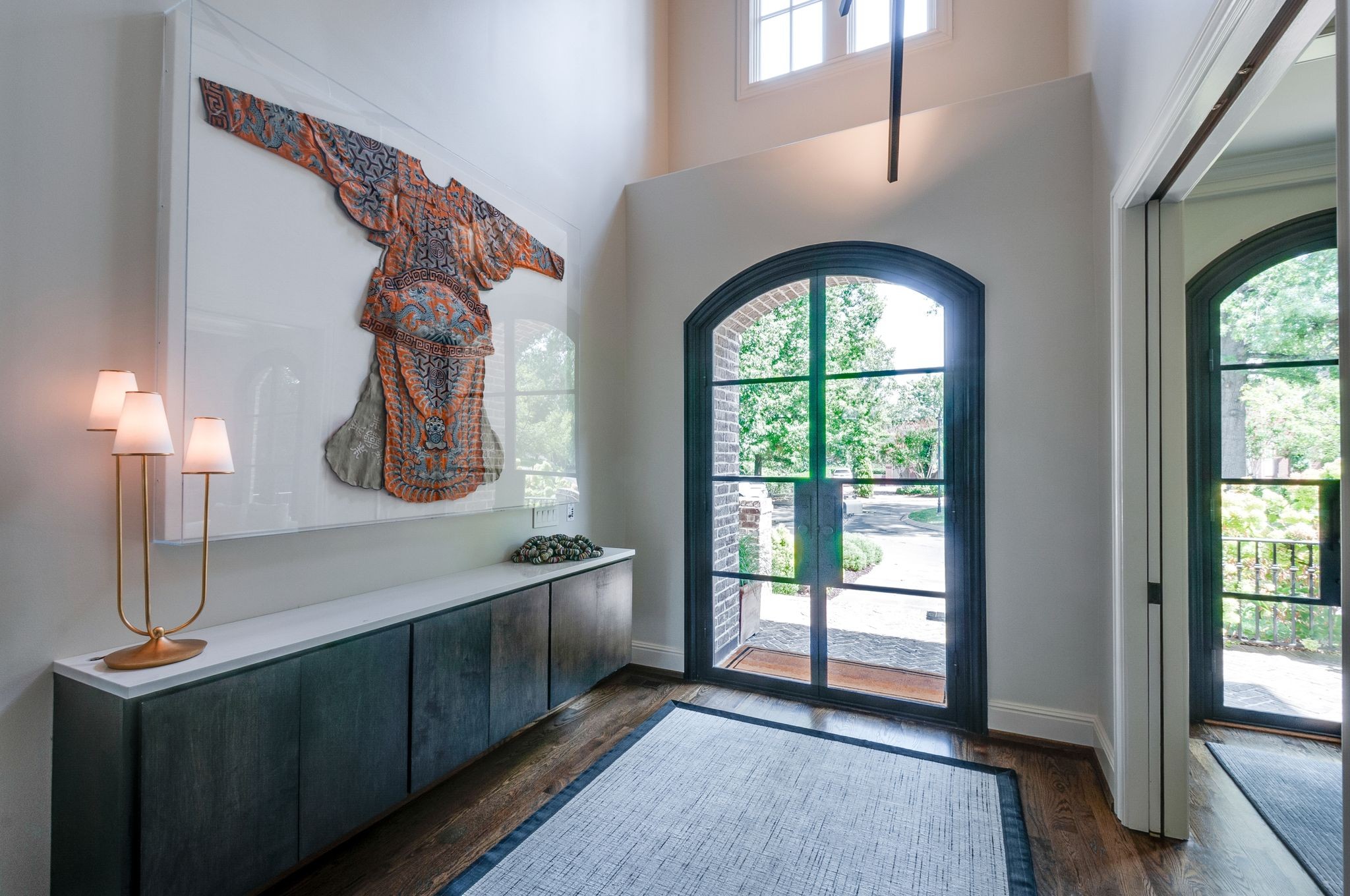 Foyer with colorful textile artwork, a long console, and tall arched glass doors.