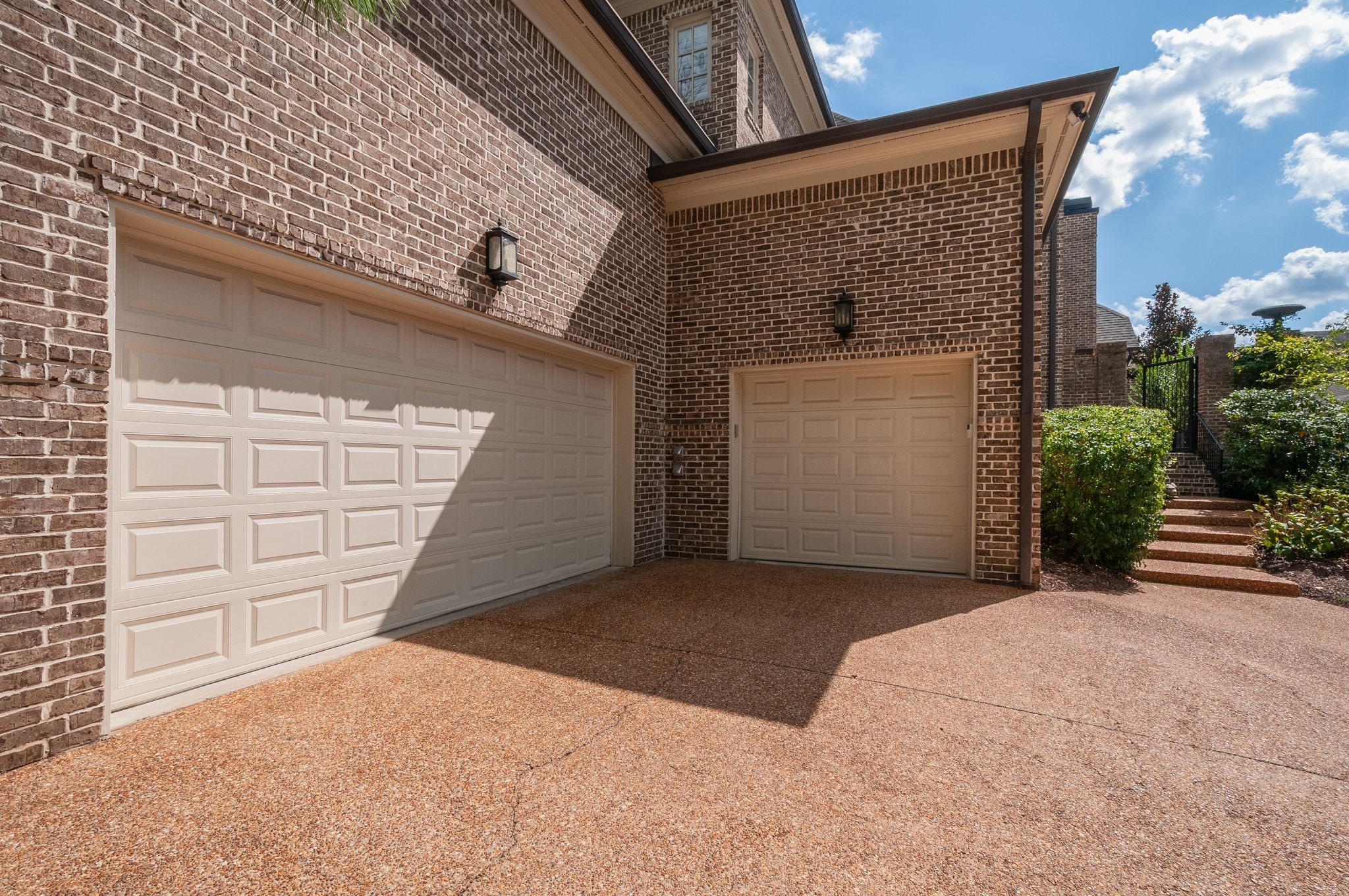 Brick house exterior with two garage doors, a wide driveway, and a gated side path.