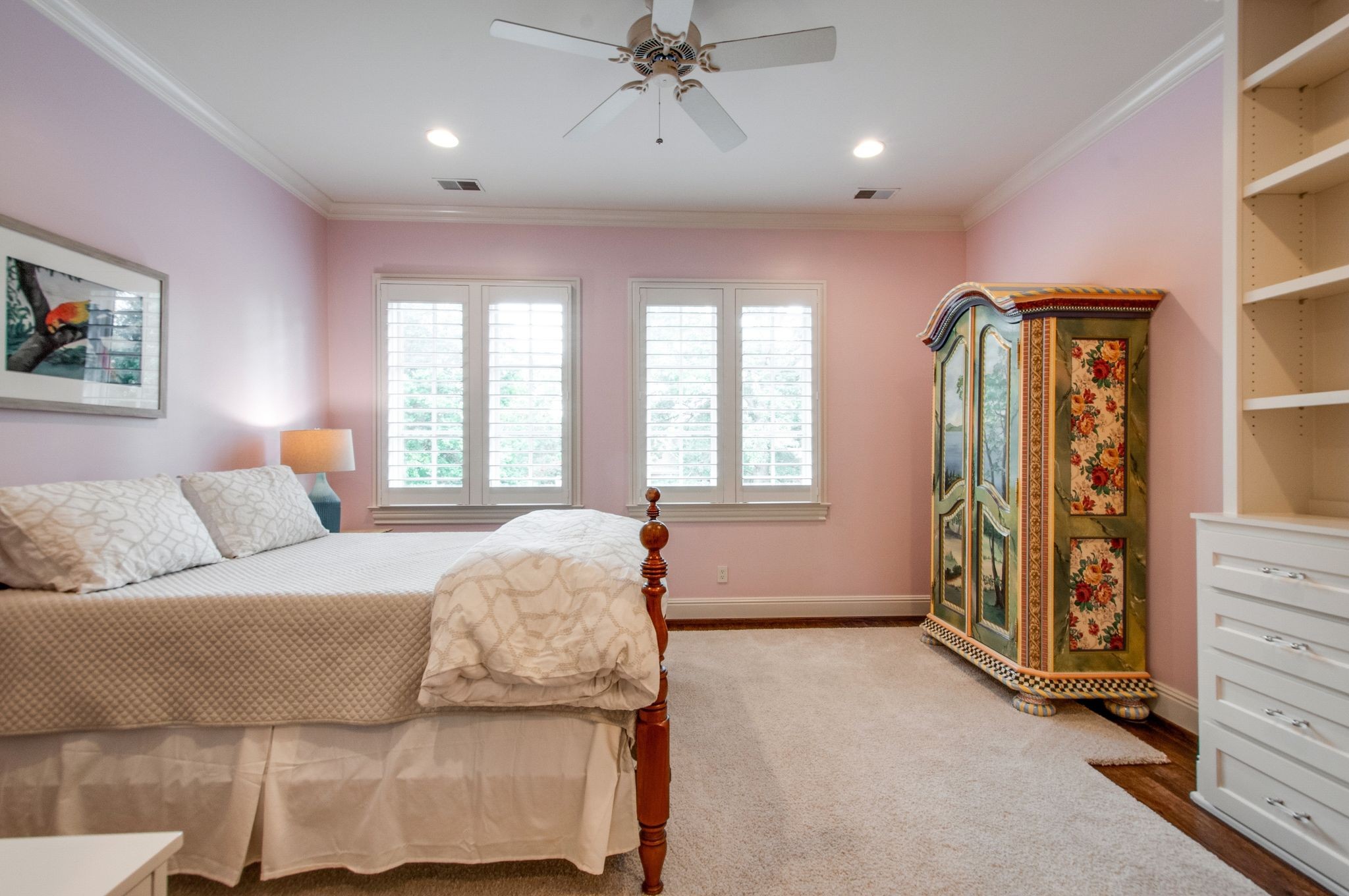 Bedroom with pink walls, a wooden bed, shuttered windows, and an ornate floral armoire.