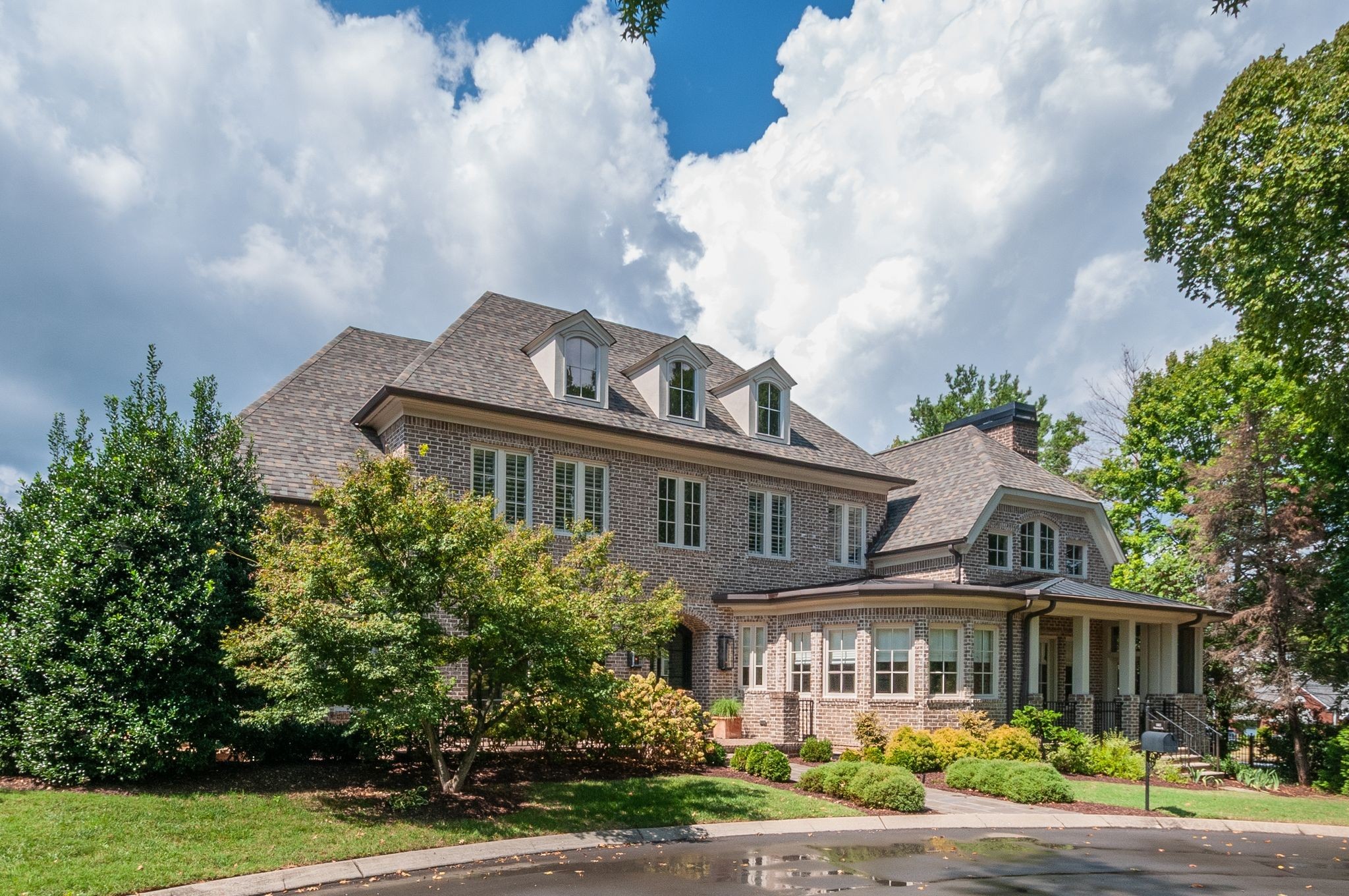 Brick home with three dormers, a covered porch, and landscaped yard.