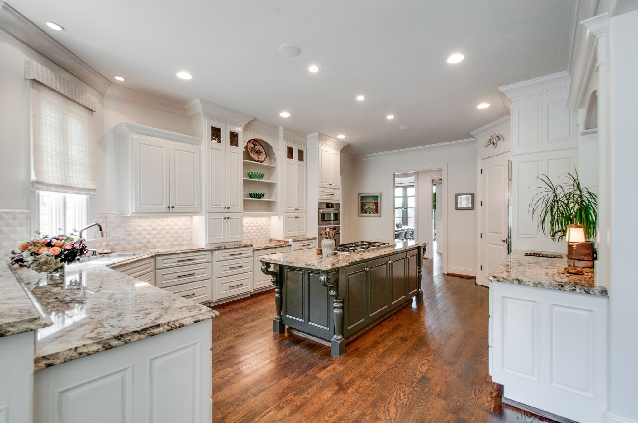 Kitchen with a dark island, gas cooktop, white cabinetry, granite counters, and hardwood floors.