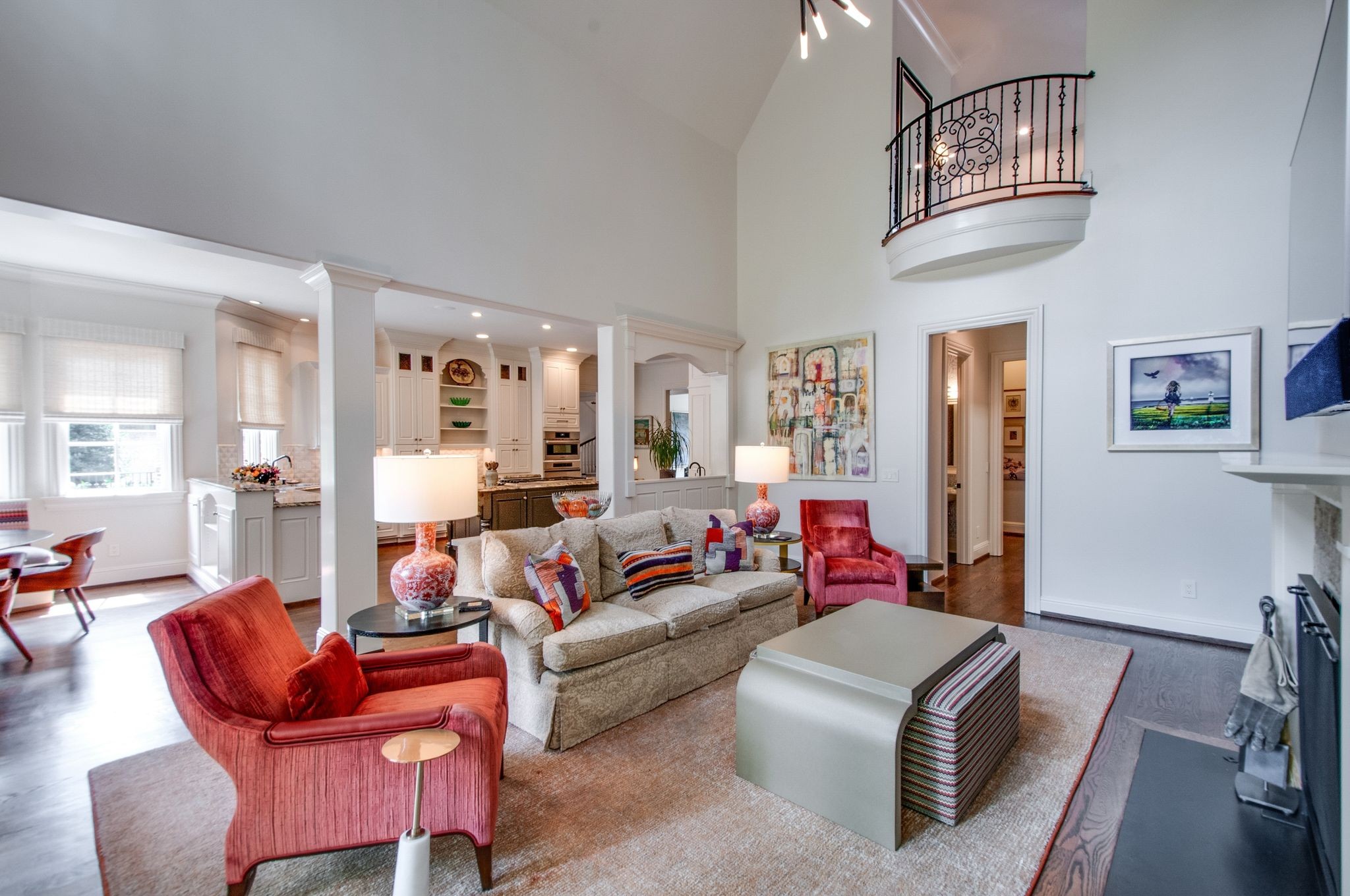 Open-plan living room with a cream sofa, red armchairs, adjoining kitchen, and ornate upper-level balcony.