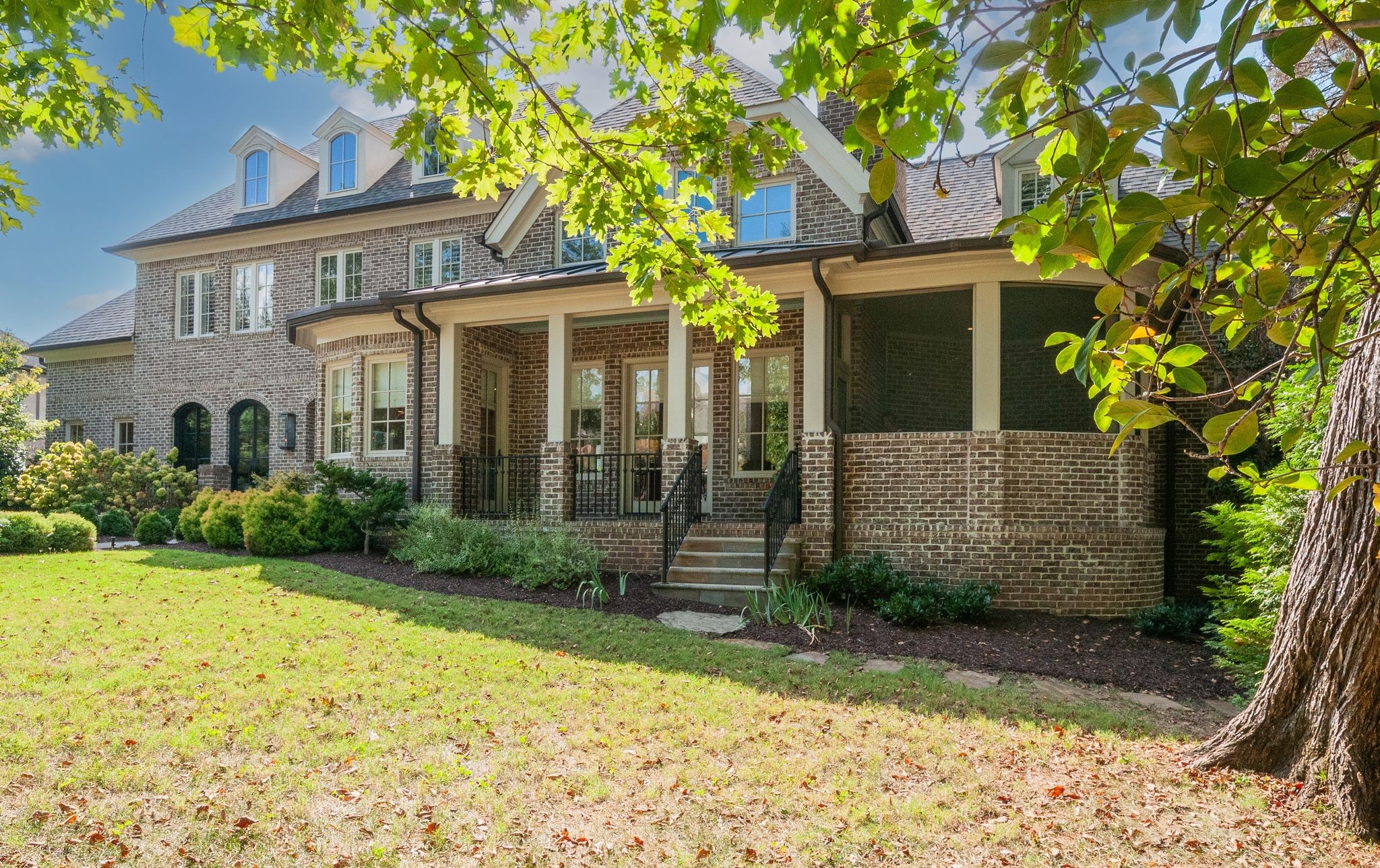 Two-story brick home with a screened porch and covered patio beneath mature trees.