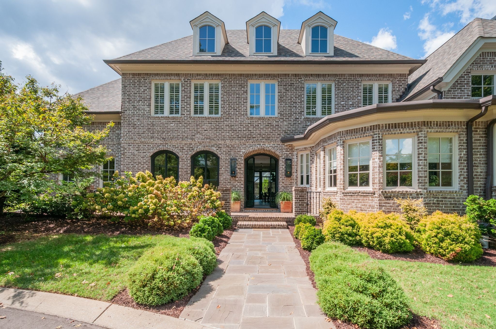 Brick home with three roof dormers, arched entry, and a landscaped walkway to the front door.