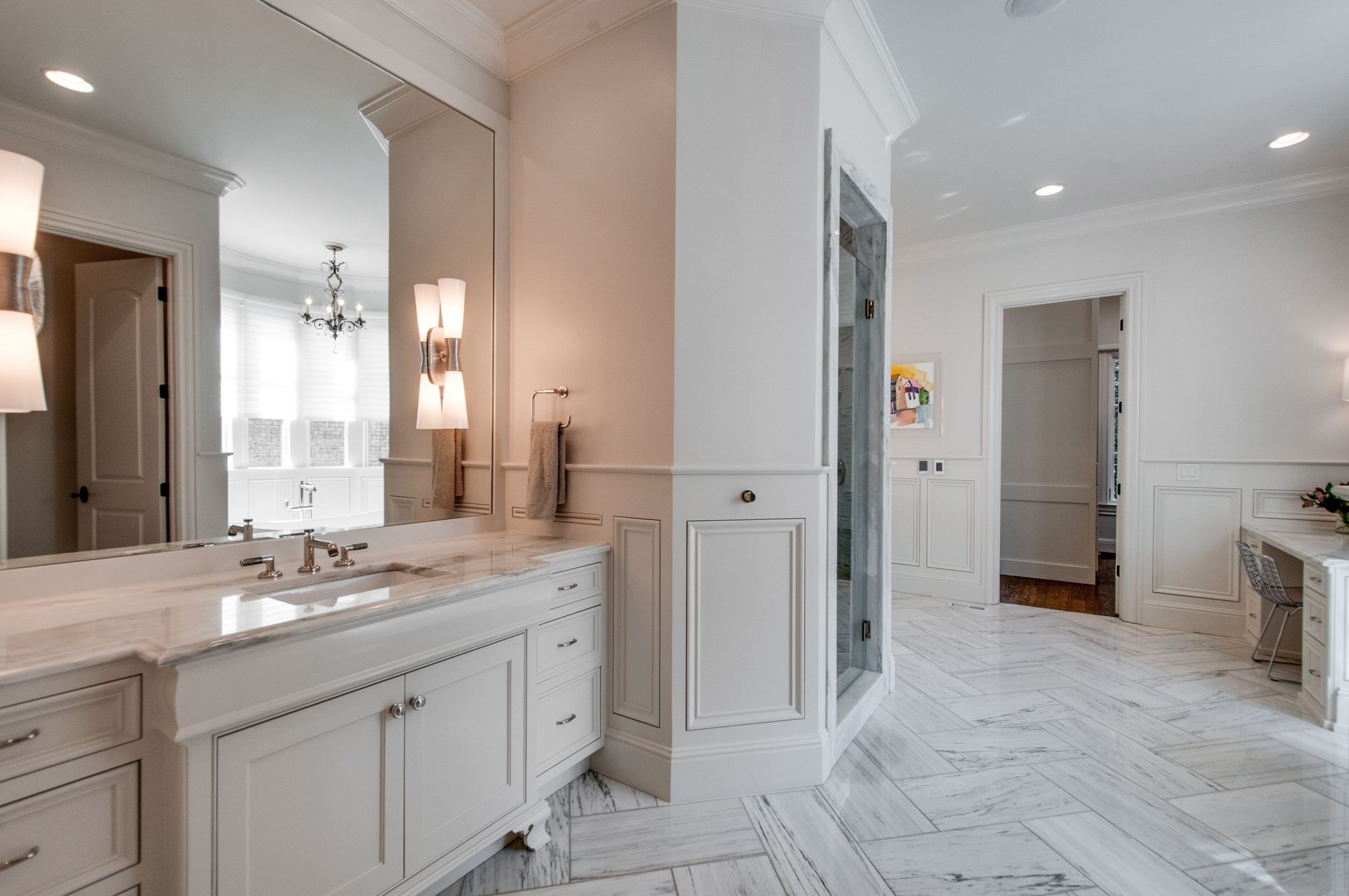 Spacious bathroom with a white double vanity, marble counters and floors, and a glass-enclosed shower.