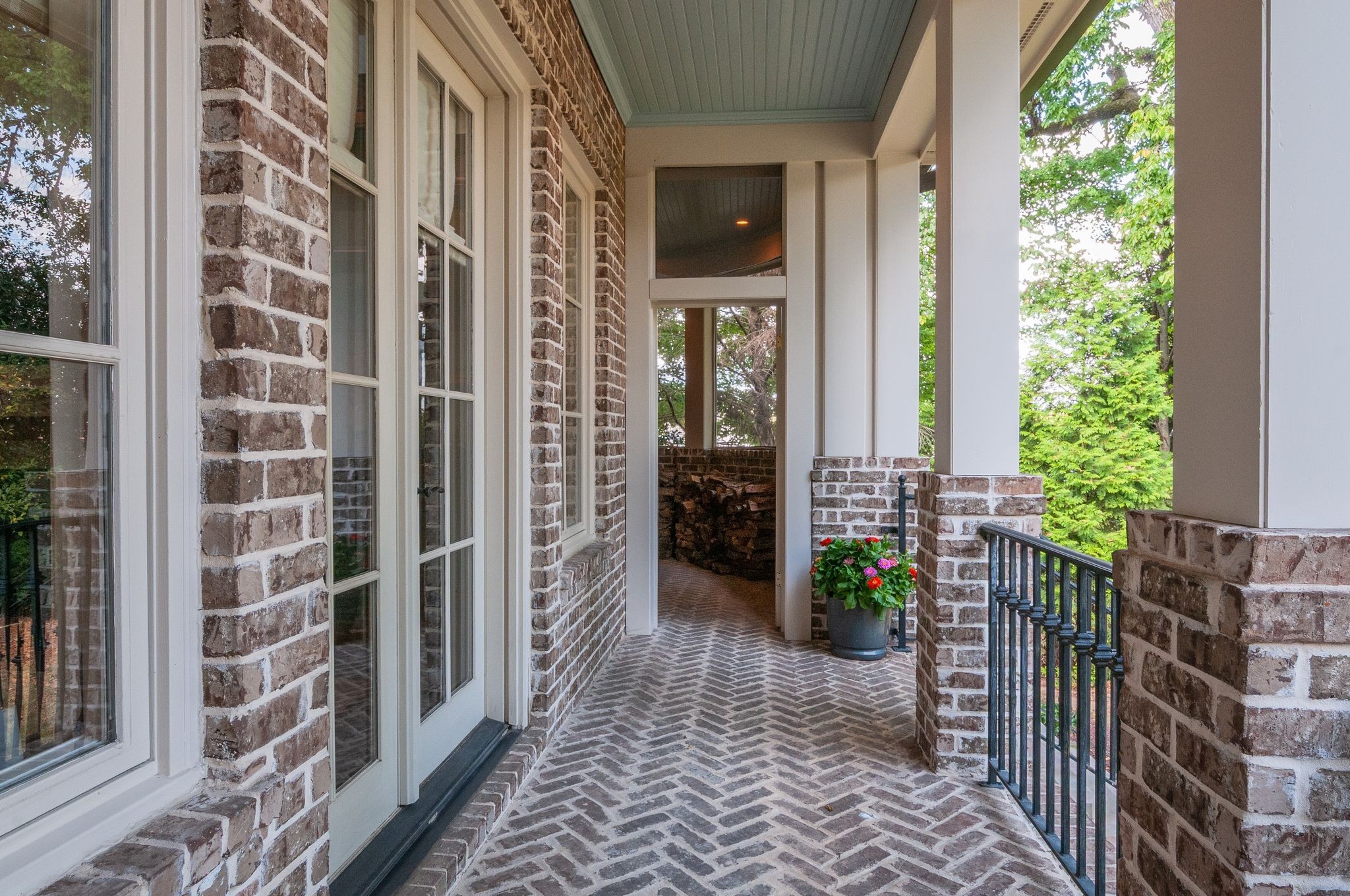 Covered brick porch with herringbone flooring, white columns, and a flower planter beside the entrance.
