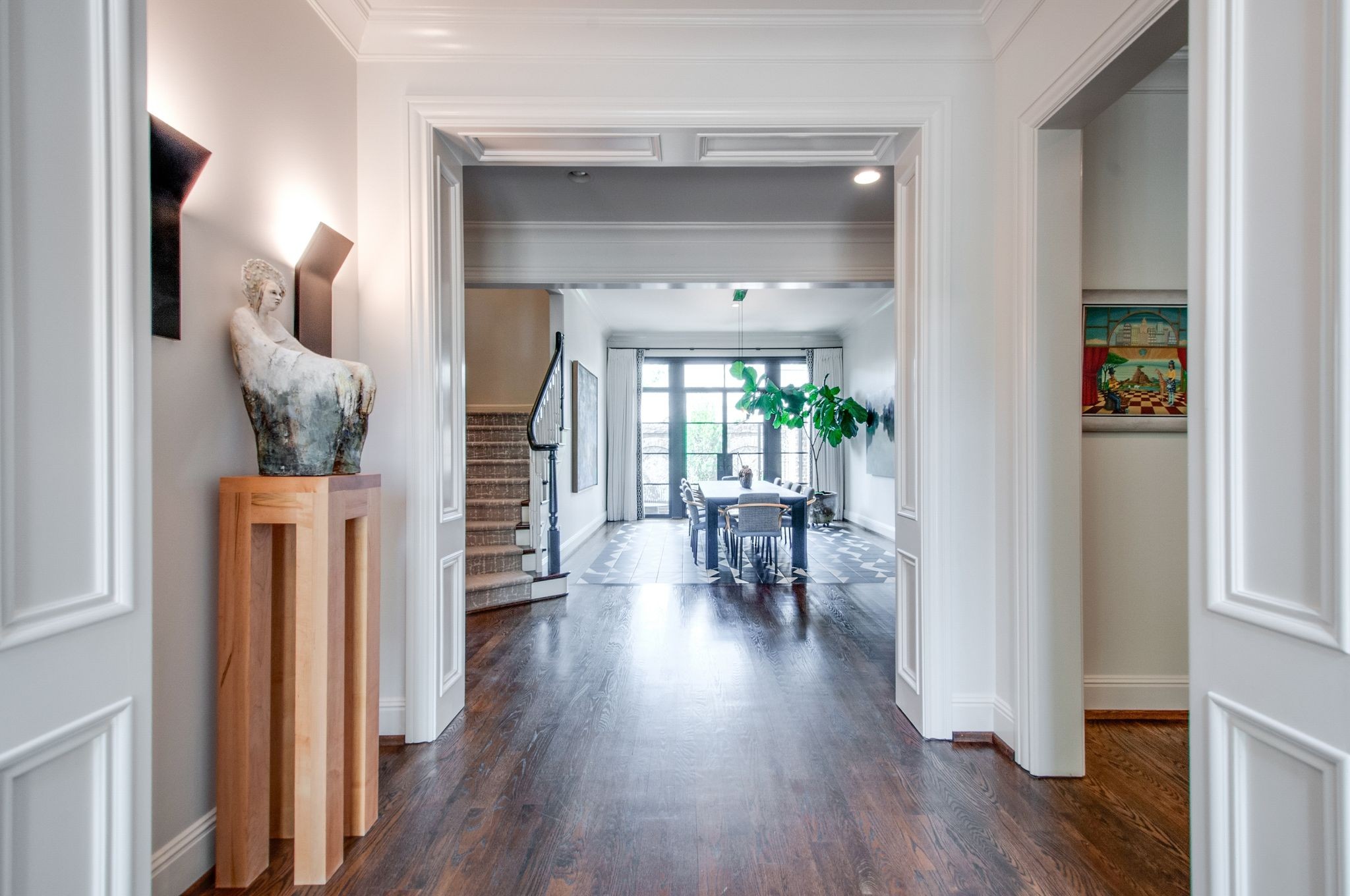 Entry hall with a sculptural figure, dark hardwood floors, and a view into the dining room.
