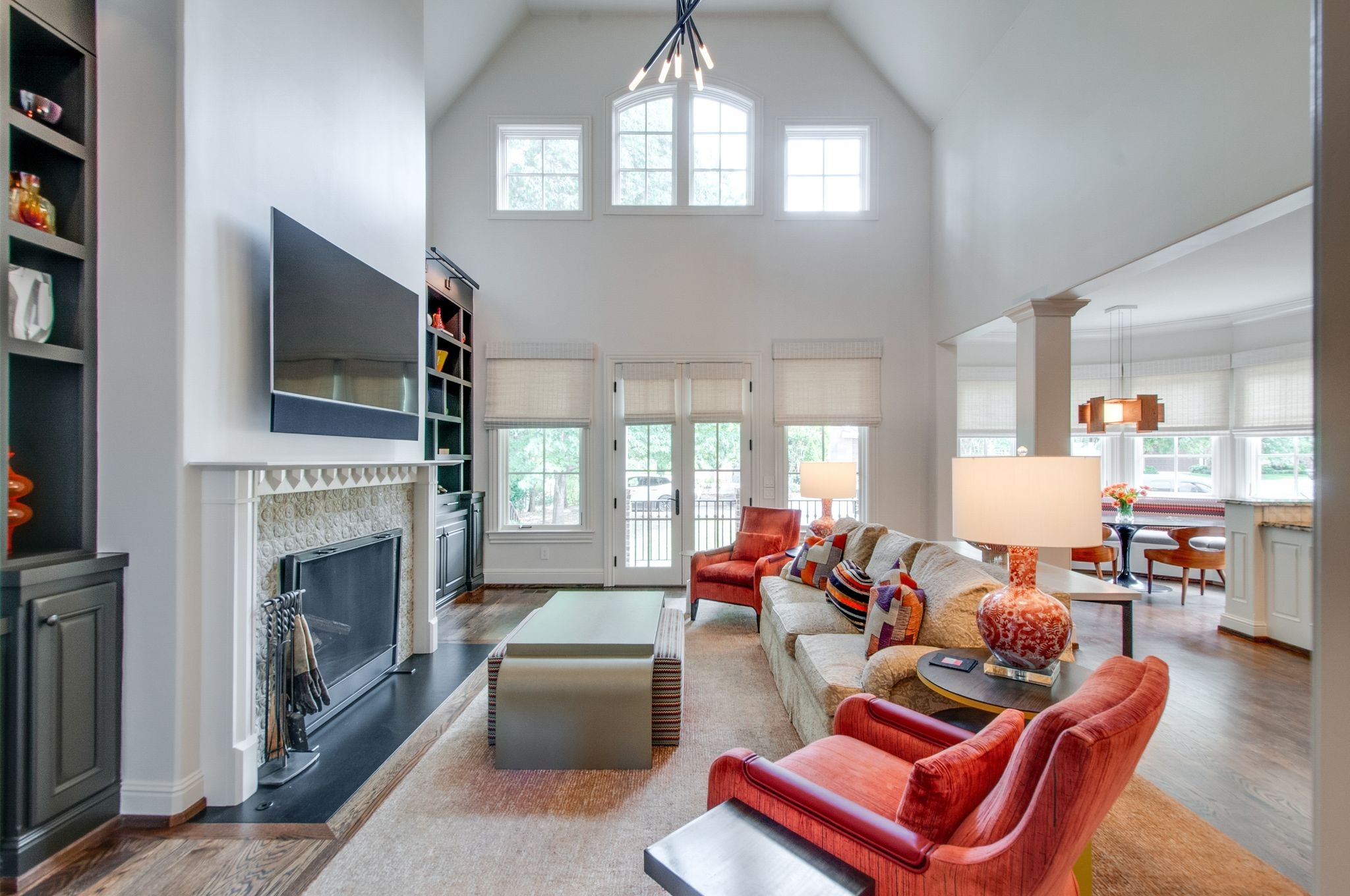 Vaulted living room with a fireplace, tall windows, built-in shelving, and red accent chairs.
