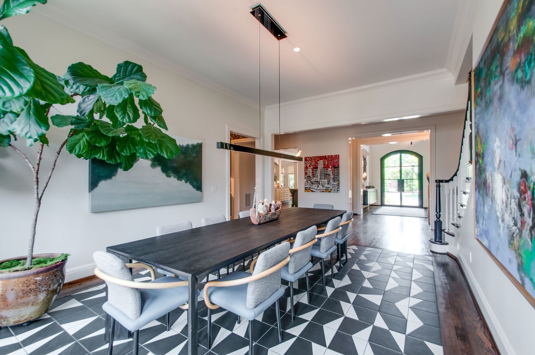 Dining room with a long dark table, geometric tile floor, potted tree, and bright arched entry door.