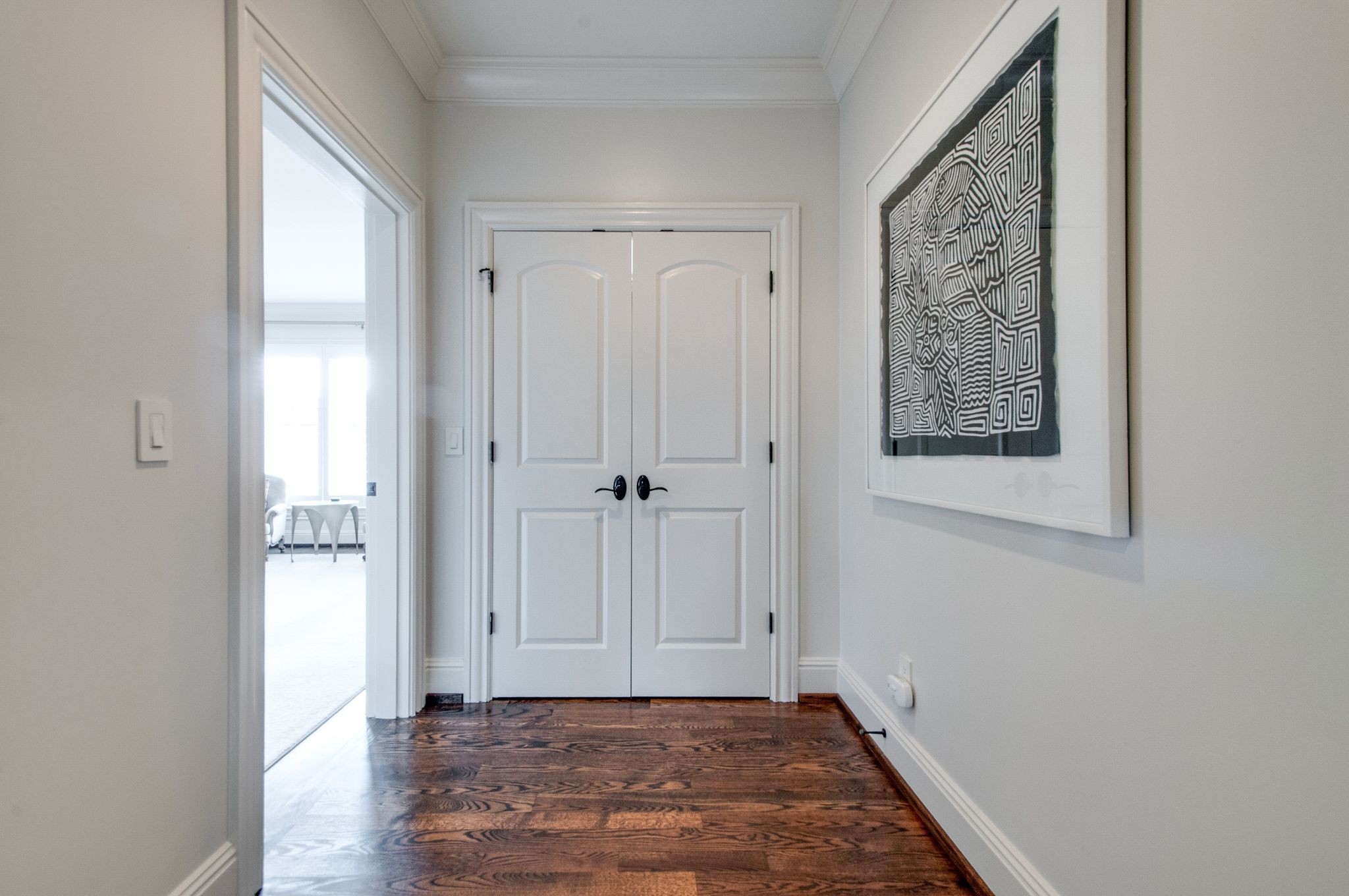 Hallway with dark hardwood floors, white double doors, and framed geometric artwork.