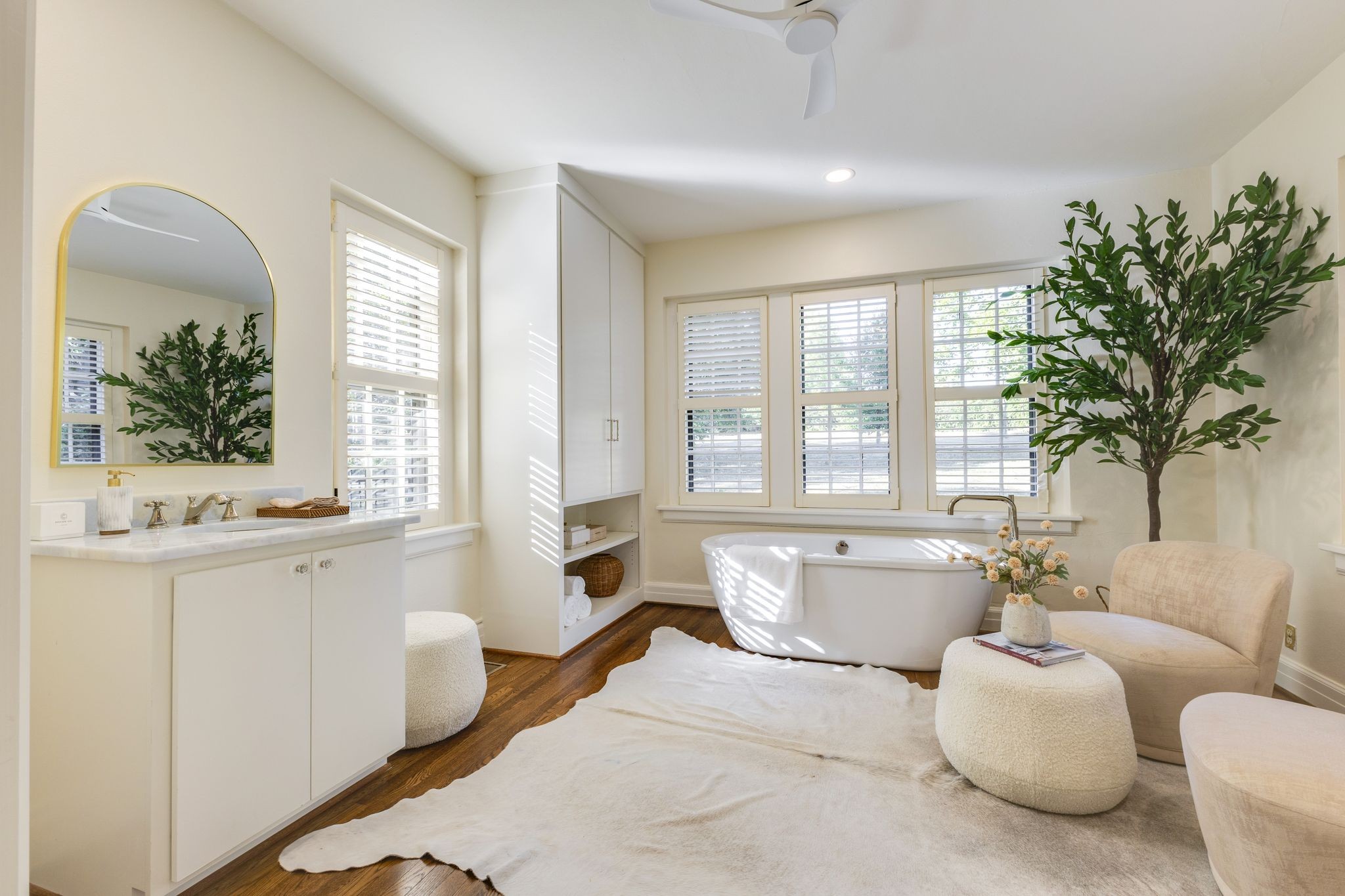 Bright bathroom with a freestanding tub, plantation shutters, and a white vanity with an arched mirror.