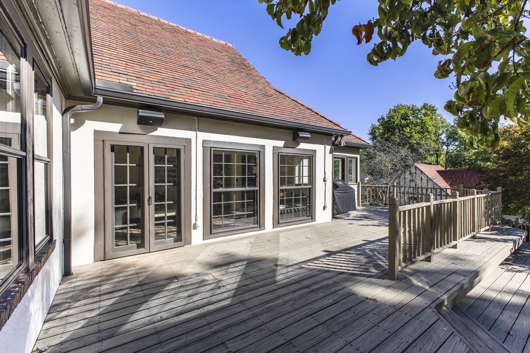 Wooden deck beside a light-colored home, with French doors, railing, and a covered grill.