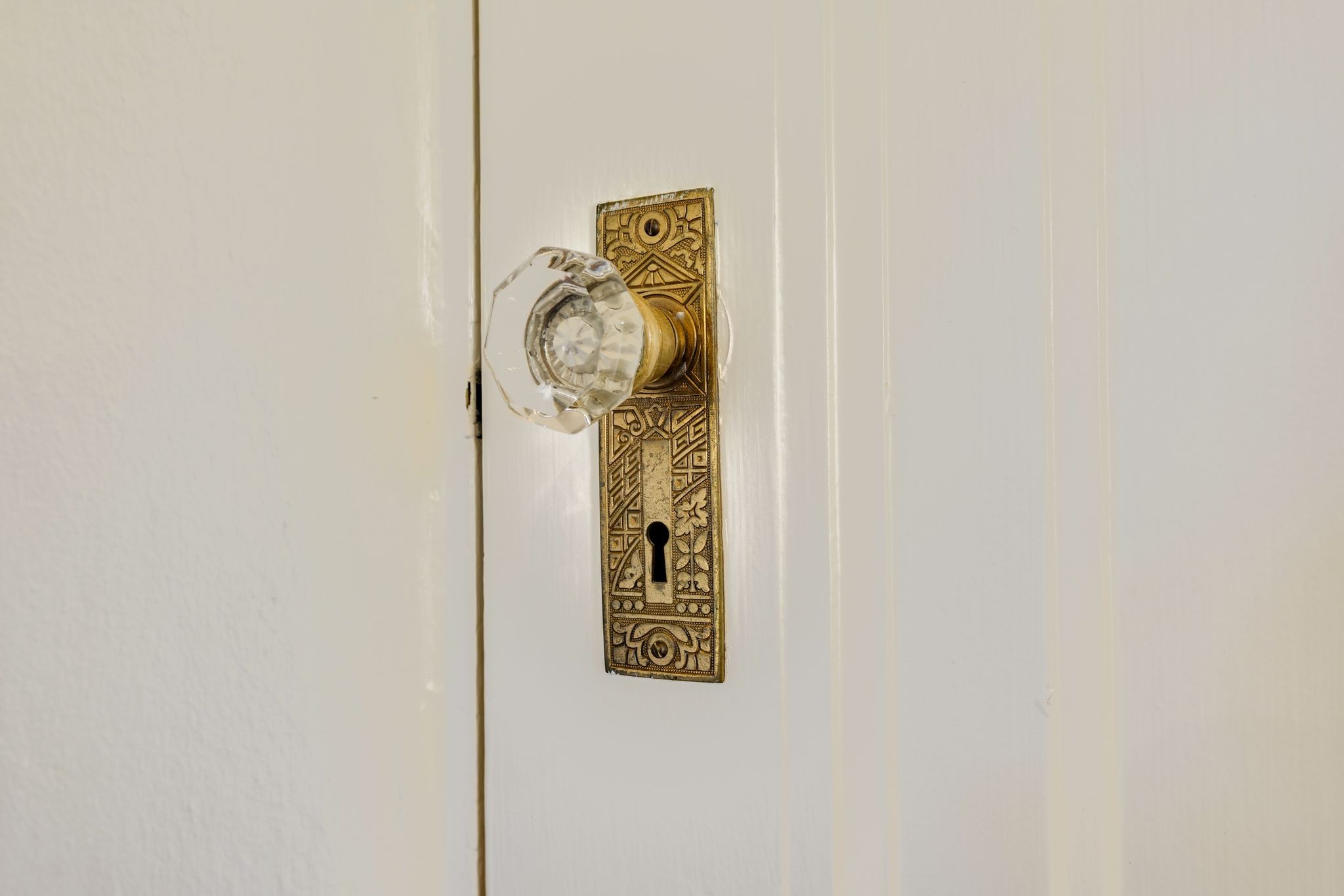Ornate brass door plate and glass doorknob on a white paneled door.