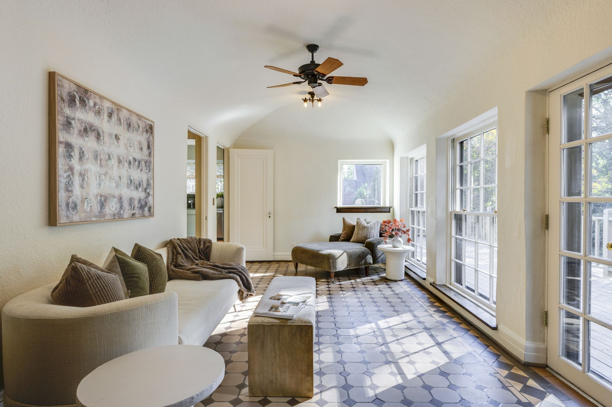 Bright sitting room with vaulted ceiling, patterned tile floor, and large windows overlooking a deck.