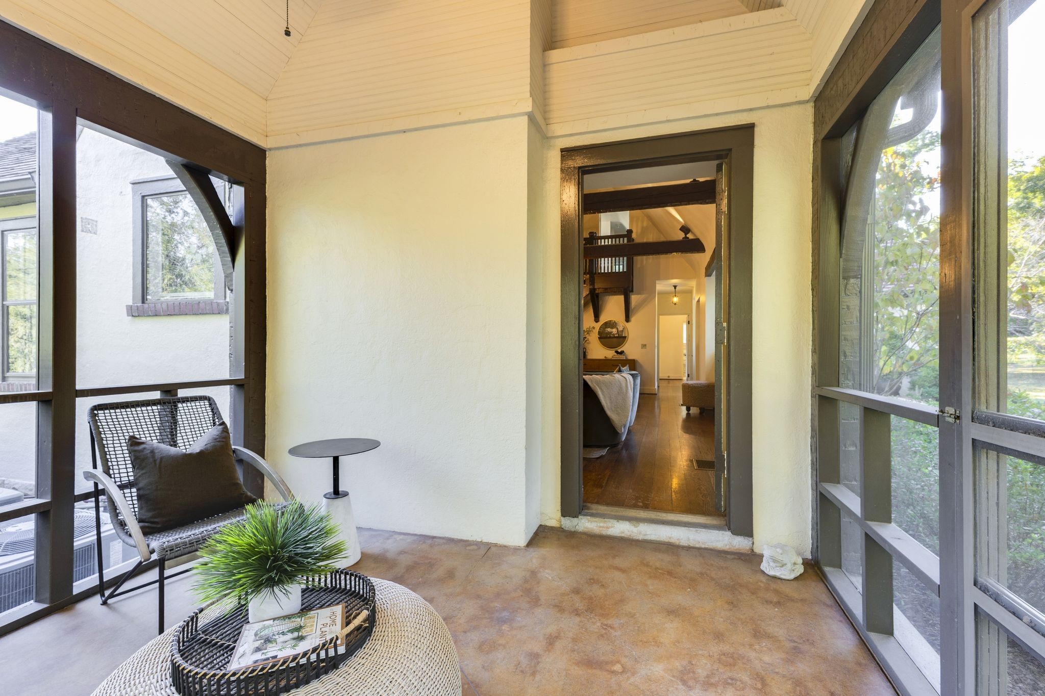 Screened porch with wicker seating and broad windows, opening into the home.