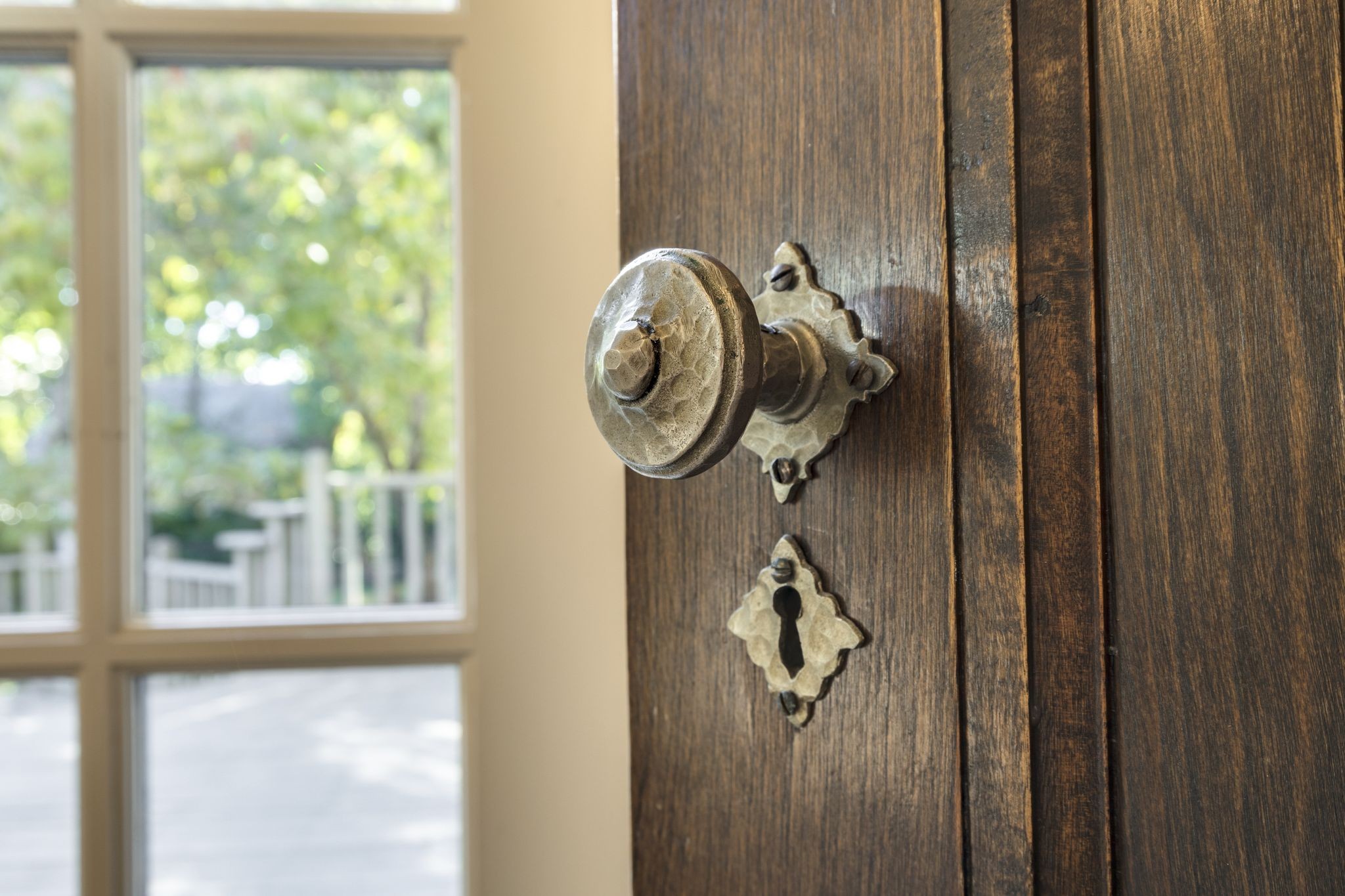 Dark wooden door with an ornate metal doorknob and keyhole beside a bright window.