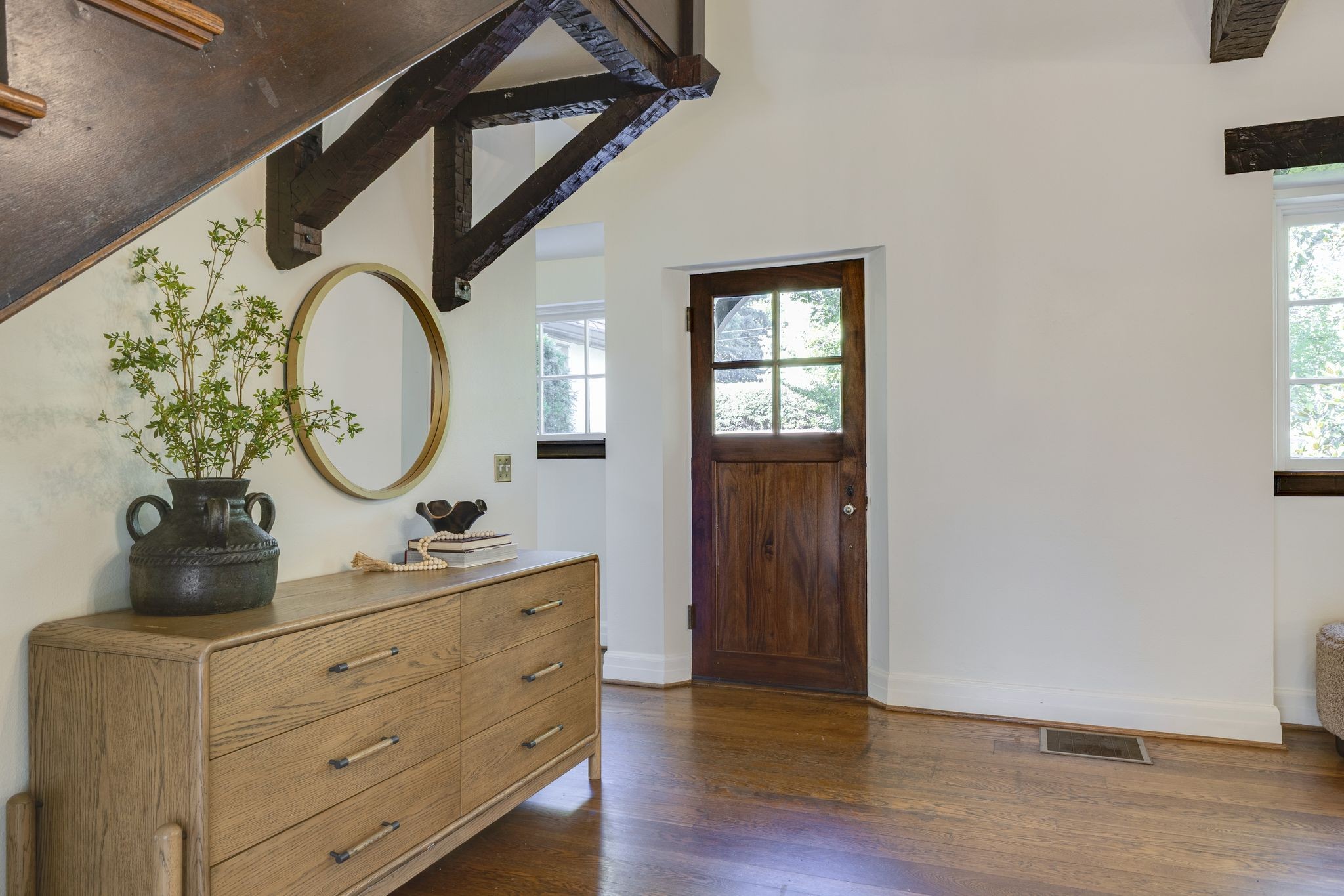 Entry hall with a dark wood front door, exposed beams, and a dresser against the wall.