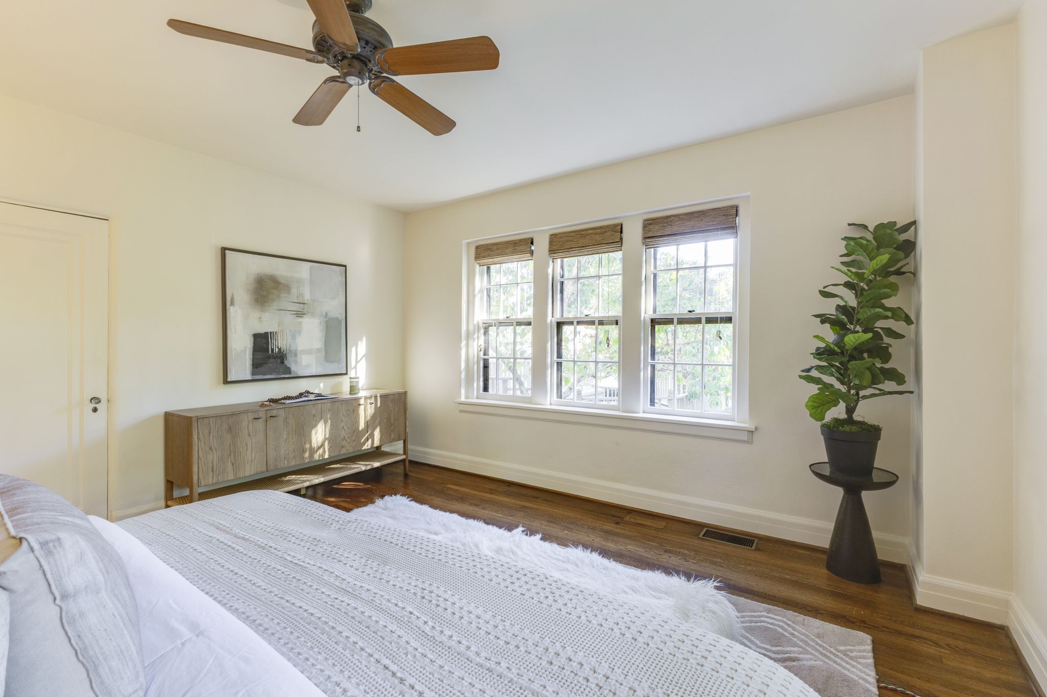 Bright bedroom with three shaded windows, a wood sideboard, and a ceiling fan.