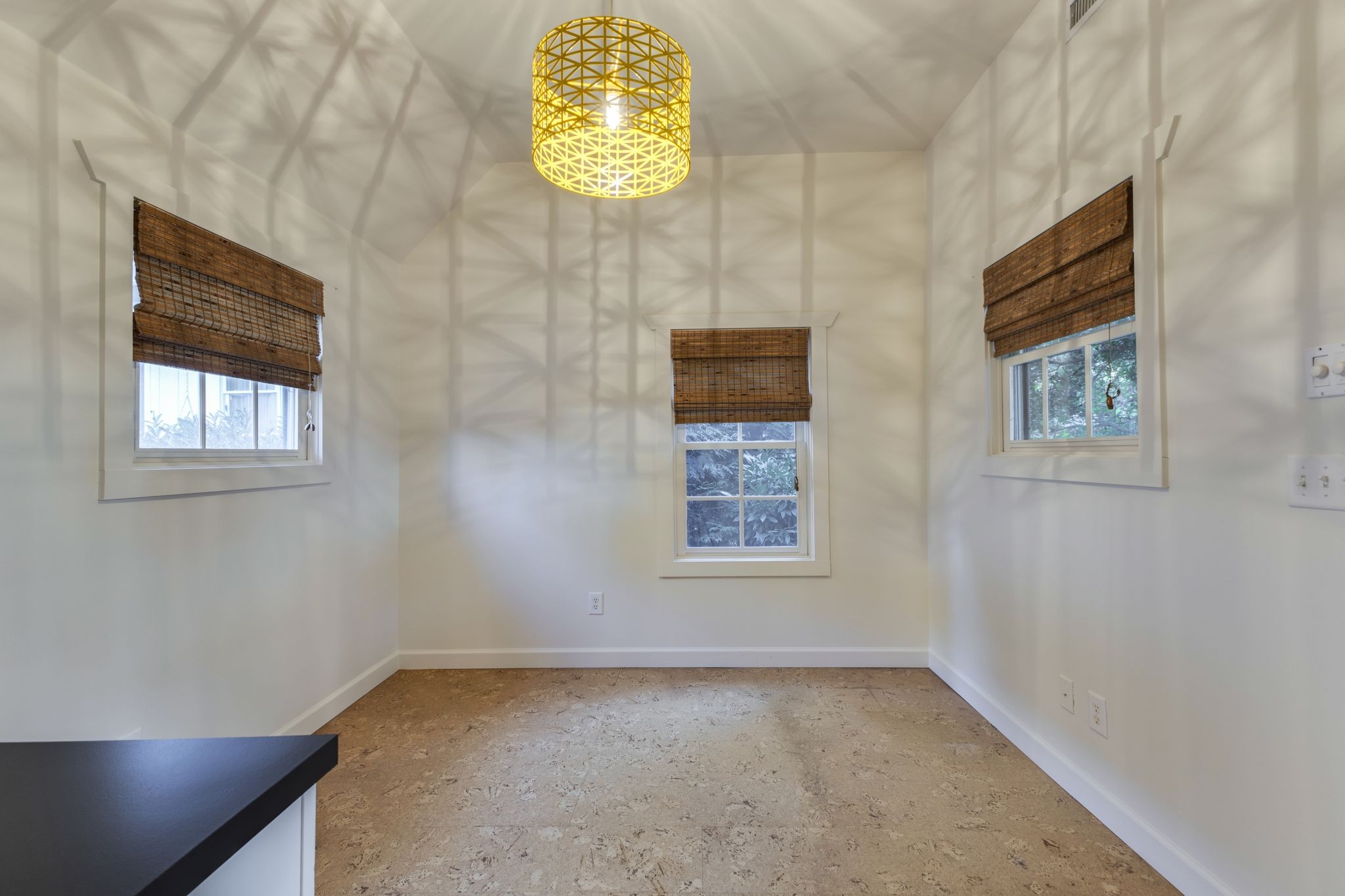 Unfurnished room with cork flooring, three shaded windows, and a yellow woven pendant light.