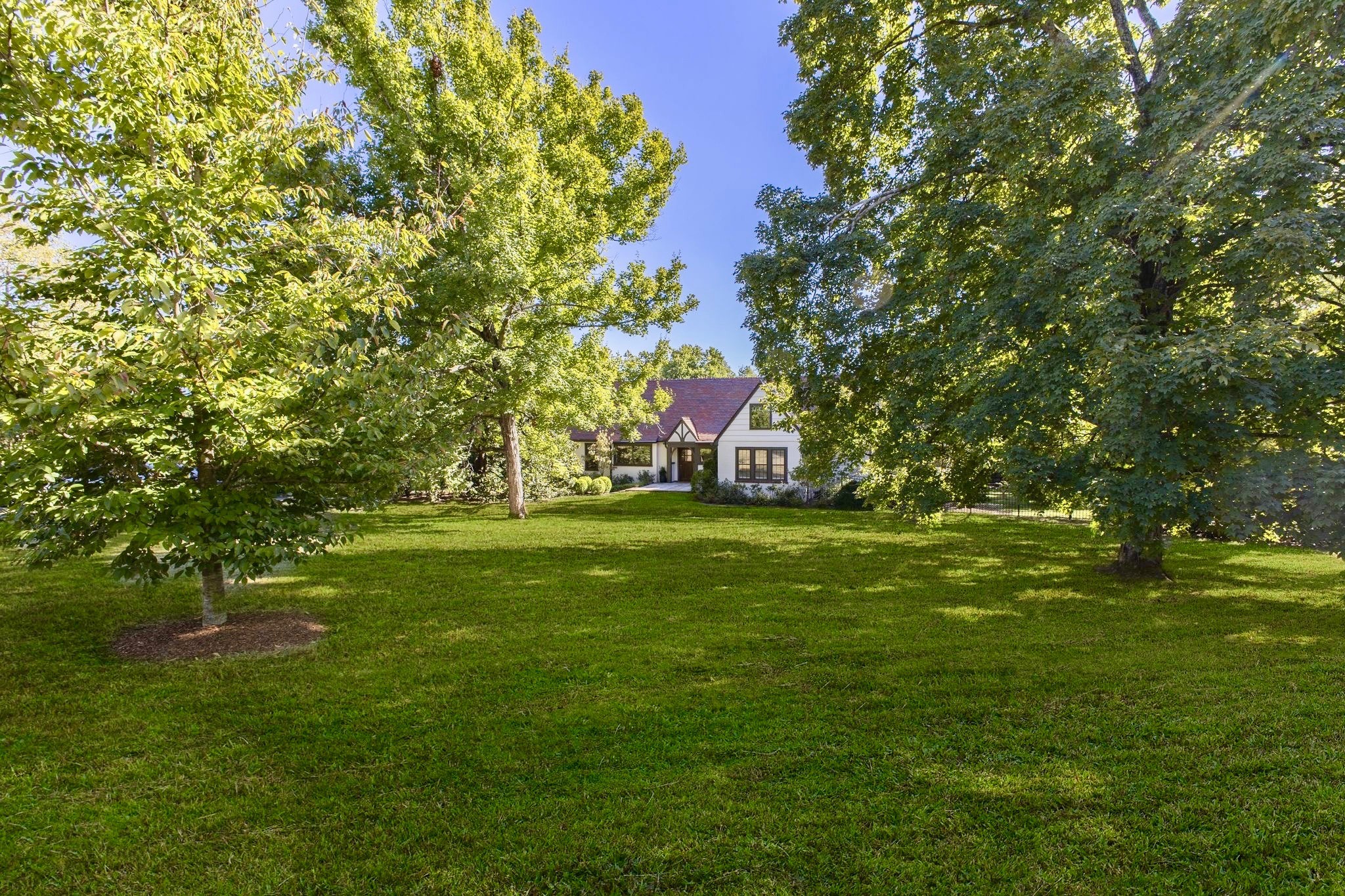 White house set beyond a broad lawn, framed by mature leafy trees.