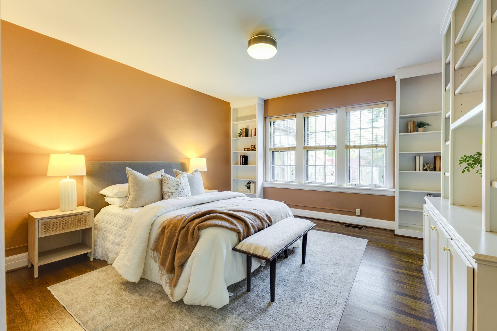 Bedroom with a white bed, built-in shelves, and three bright windows.