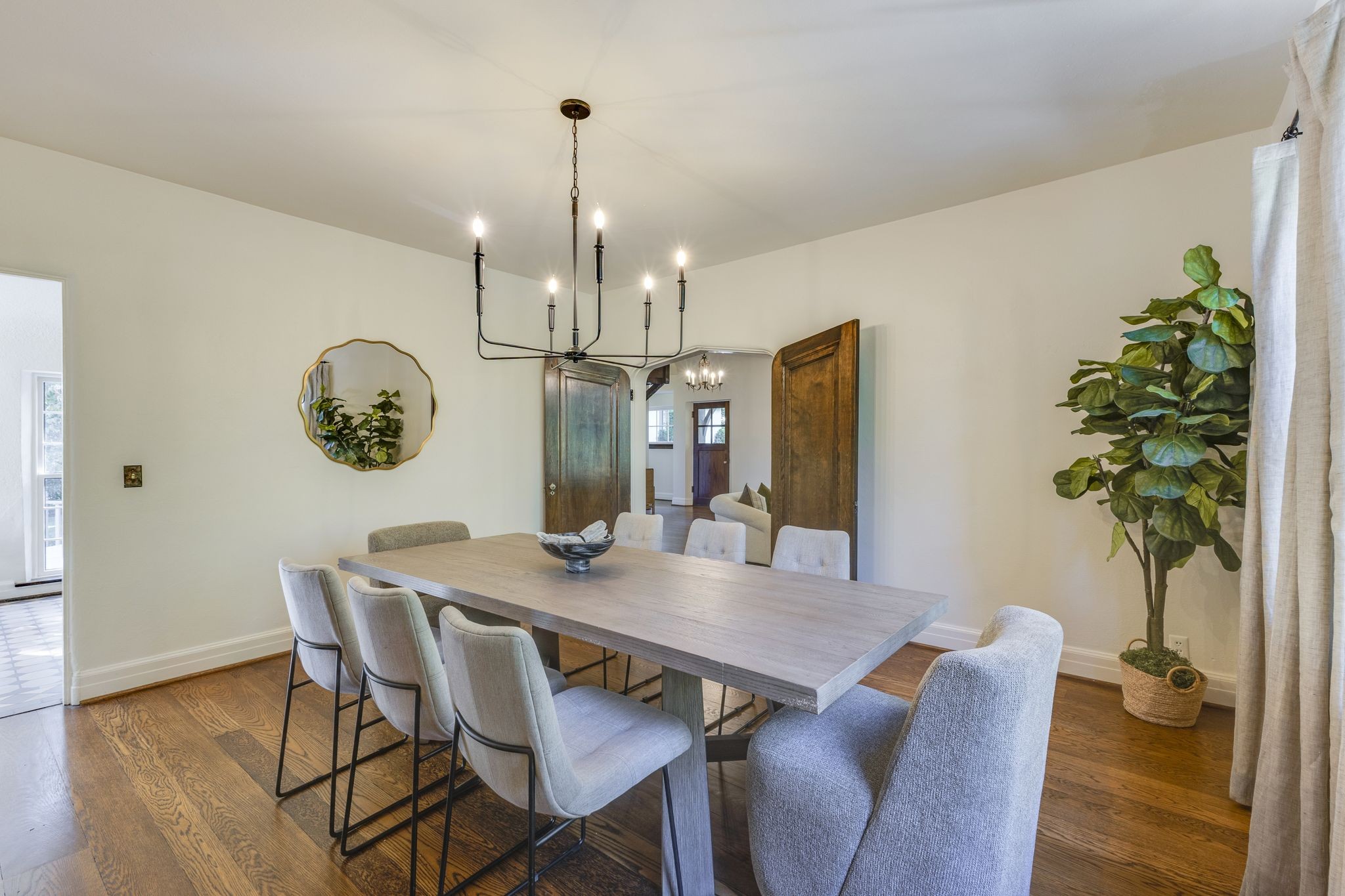 Dining room with a long gray table, upholstered chairs, and a black chandelier over hardwood floors.