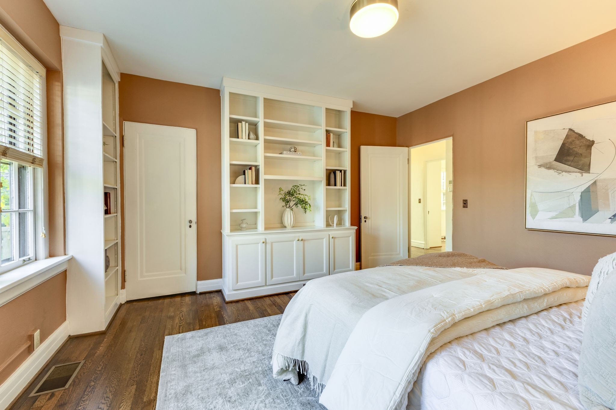 Staged bedroom with built-in white bookshelves, a white bed, and dark wood floors.