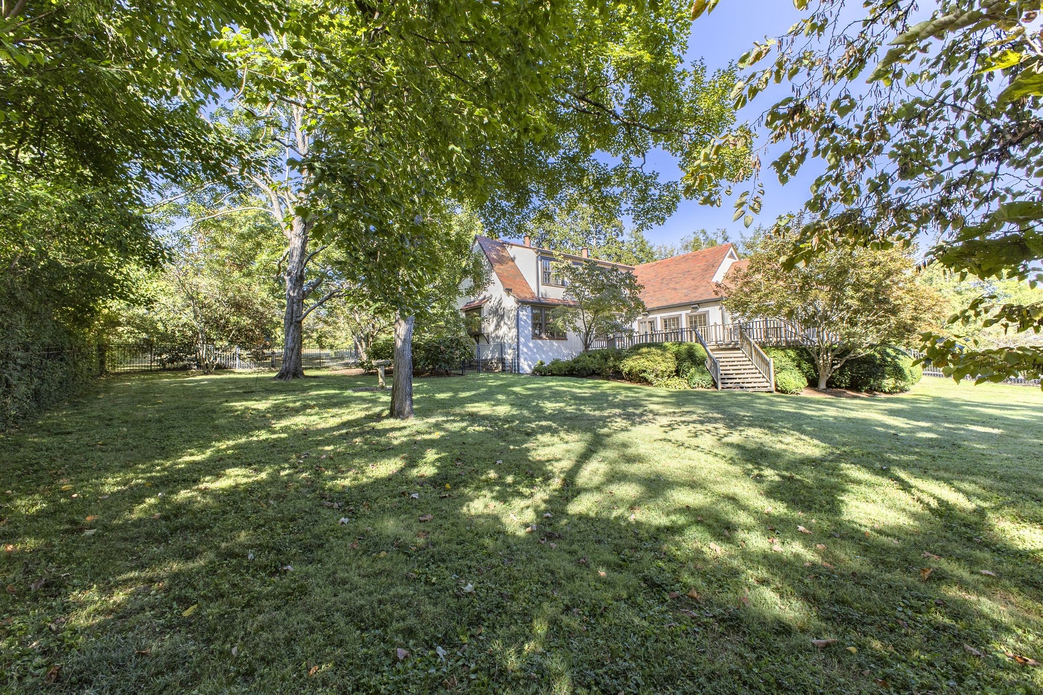 House rear with raised deck and stairs overlooking a broad lawn beneath mature trees.