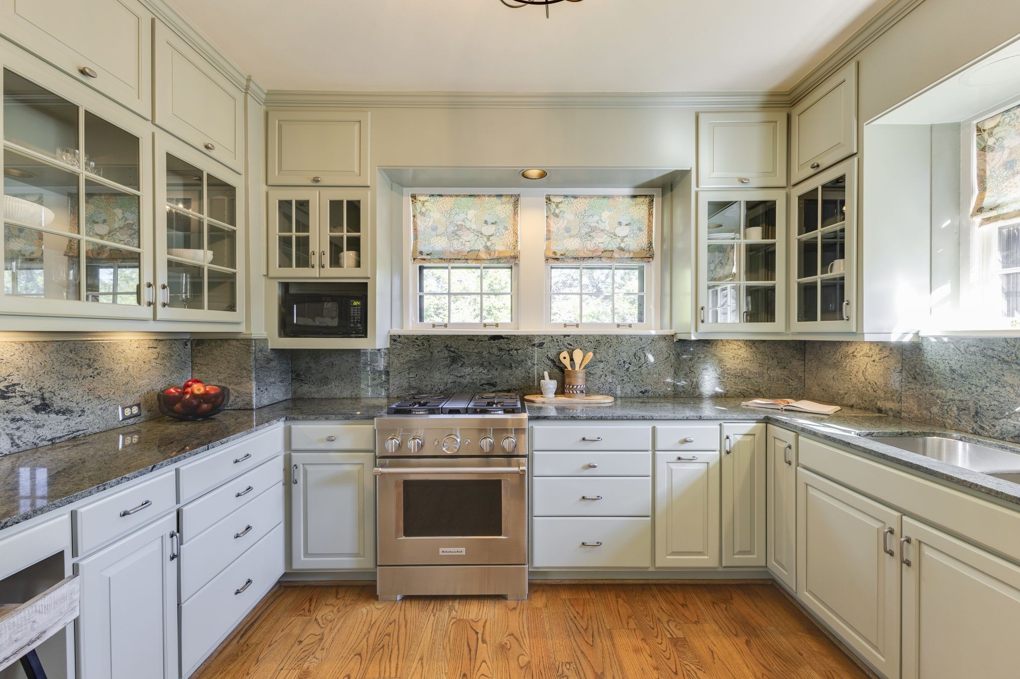 Kitchen with cream cabinets, gray granite counters, a stainless steel range, and two patterned window shades.