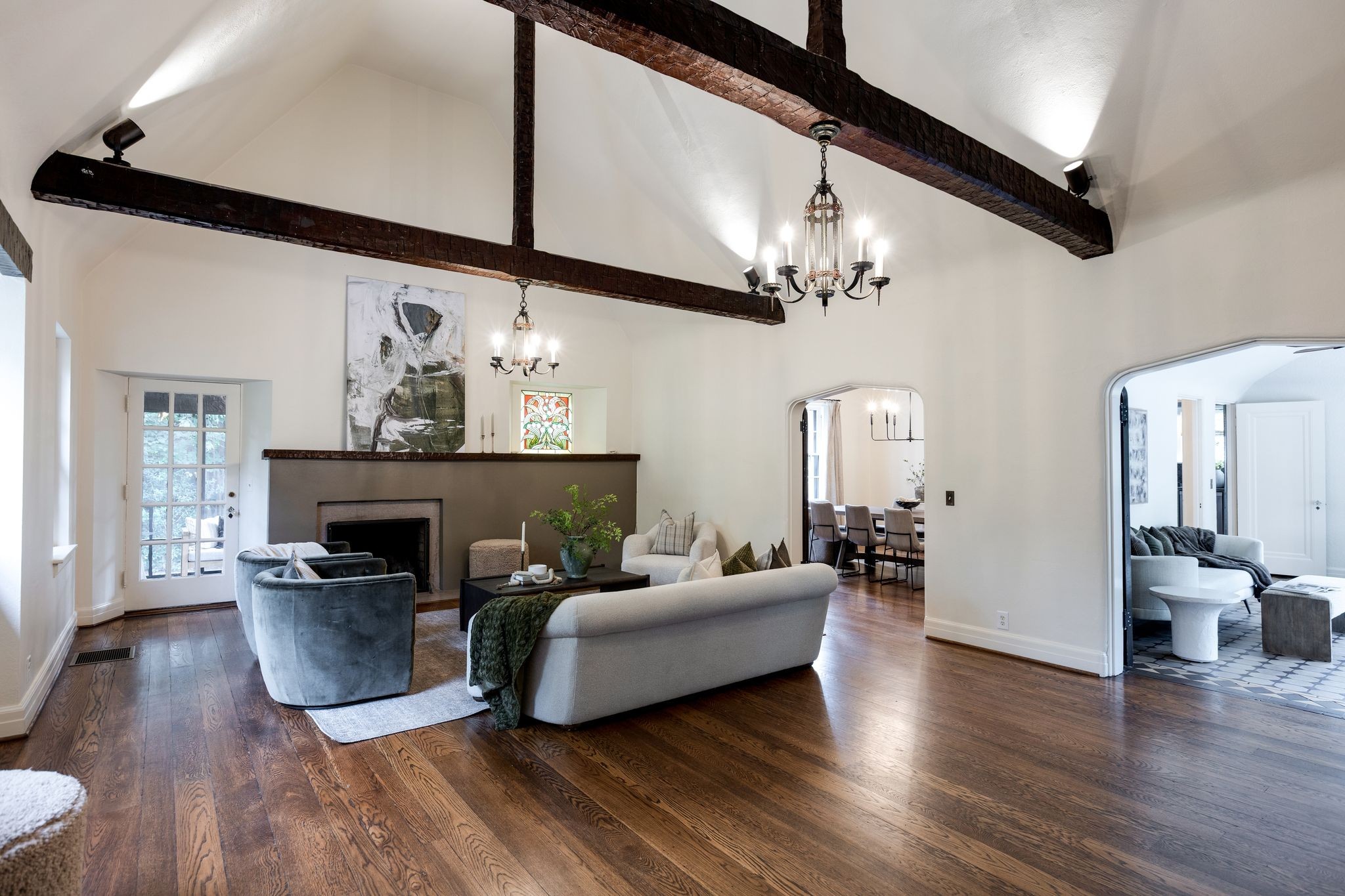 Living room with exposed ceiling beams, a fireplace, hardwood floors, and arched openings to adjoining rooms.