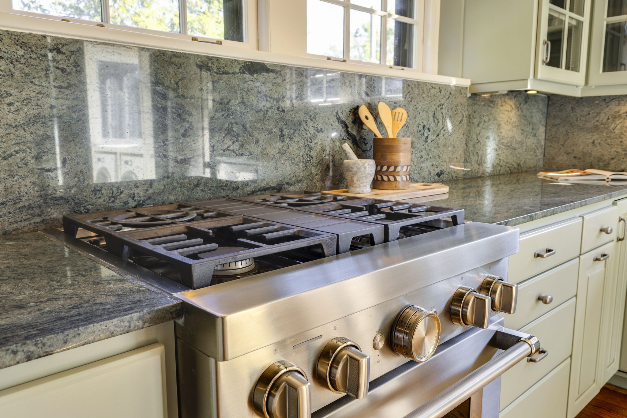 Kitchen with a stainless steel gas range and gray granite counters beneath bright windows.