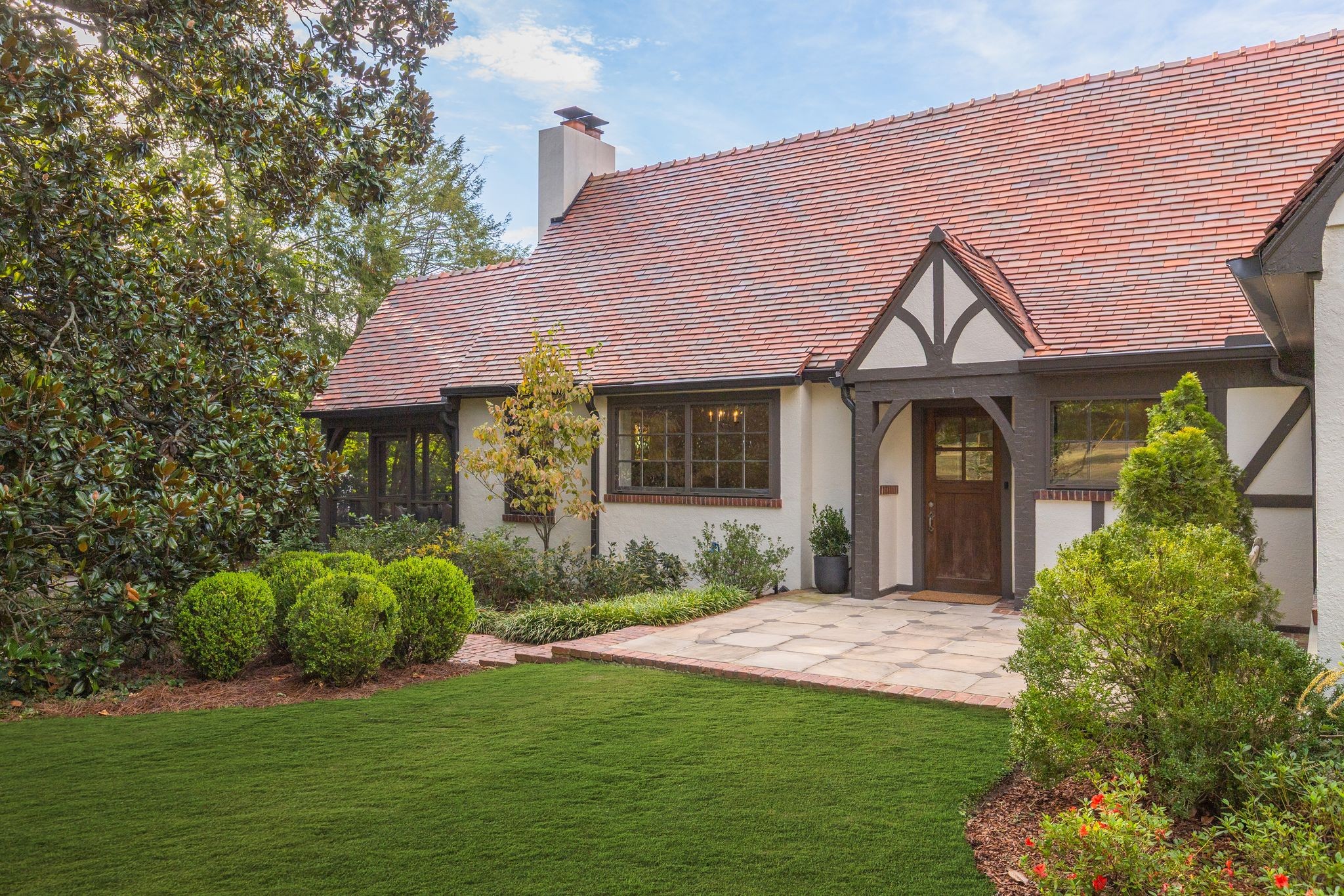 Tudor-style house with a red tile roof, timber-trimmed entry, and landscaped front lawn.